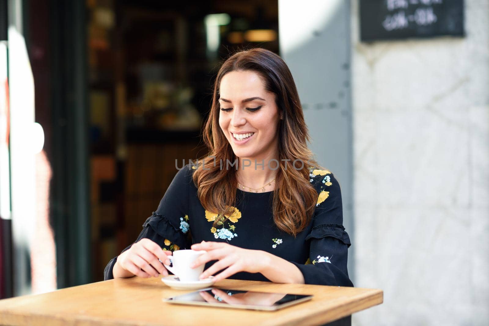 Young woman drinking coffee in an urban cafe bar. Middle-aged female sitting at table at an outside terrace. Girl with california highlights hairstyle.