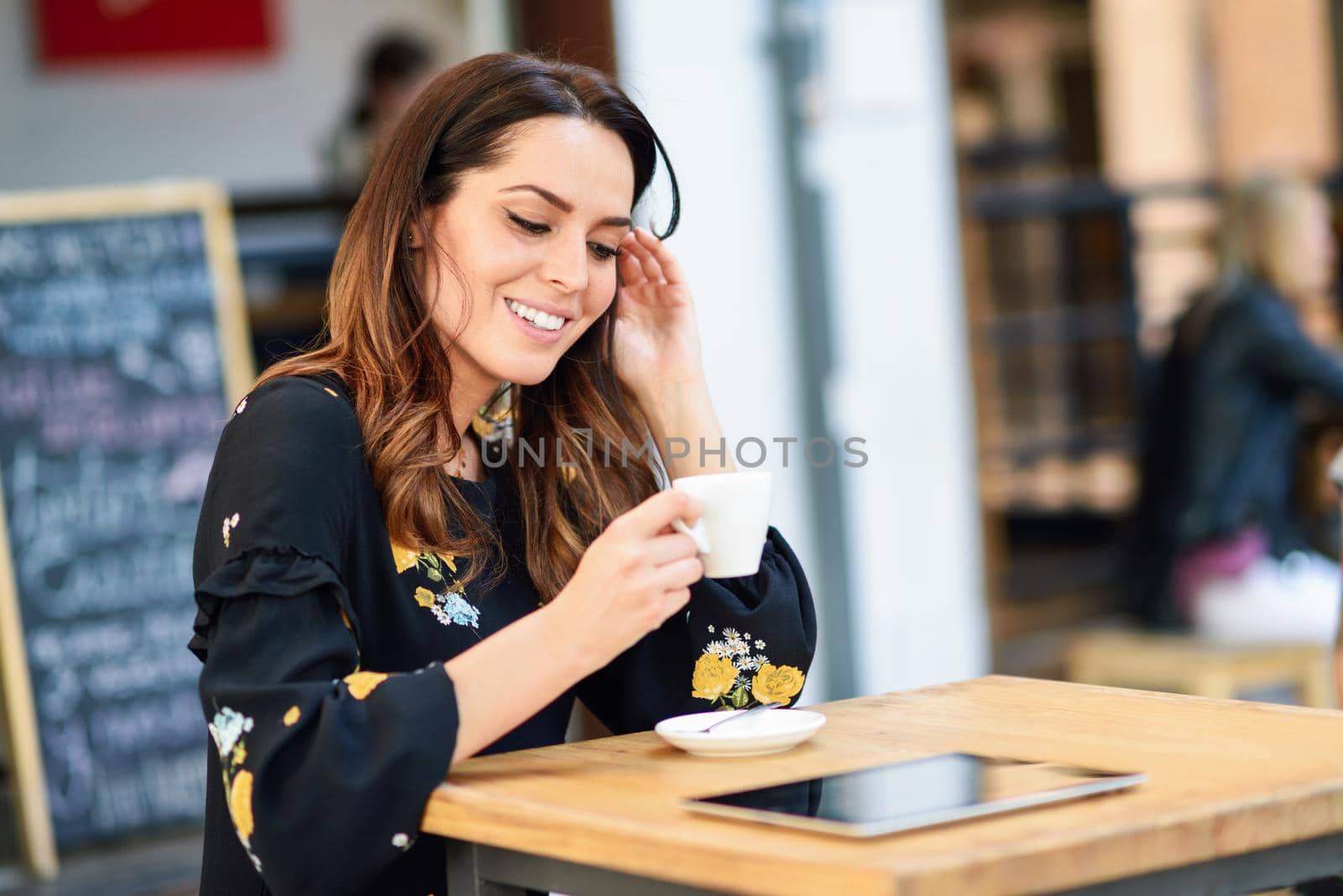 Middle-aged woman drinking coffee in an urban cafe bar. Young female sitting at table at an outside terrace. Girl with california highlights hairstyle.