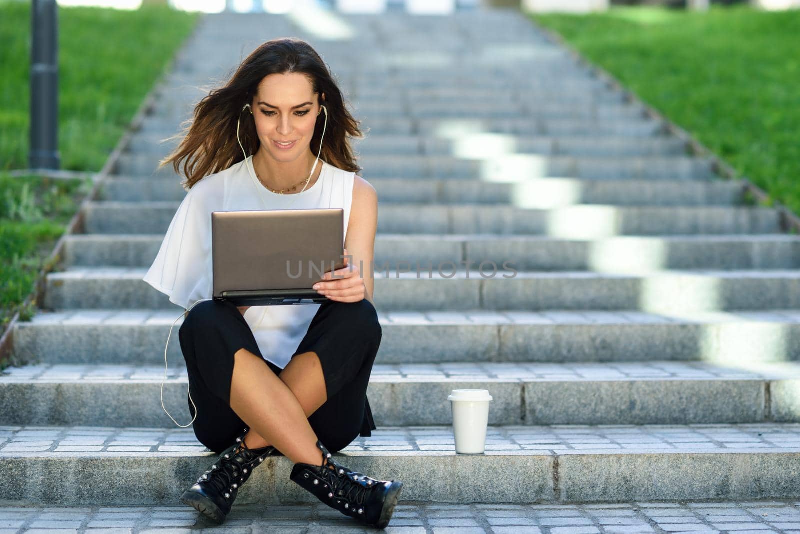 Young businesswoman having a videoconference with her laptop computer sitting on urban steps outdoors.