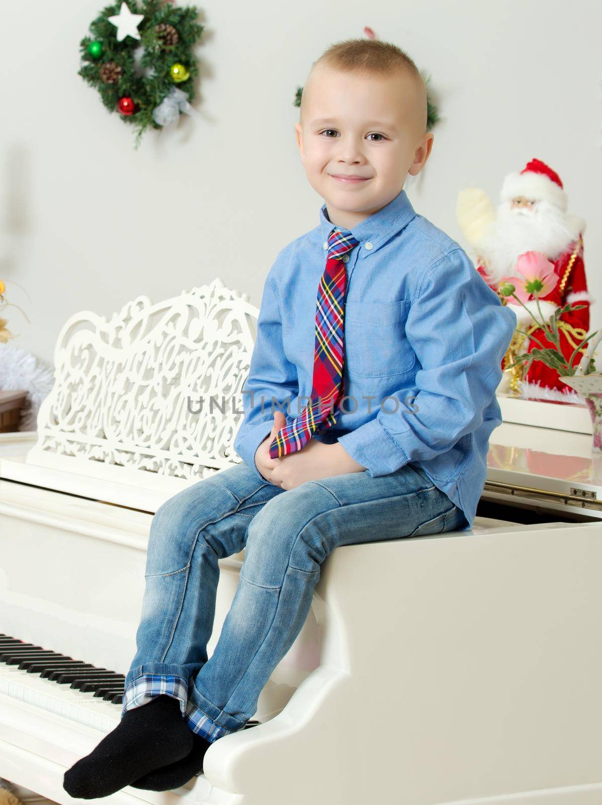 Elegant little boy in shirt and tie sitting on a white piano.In the Christmas night.