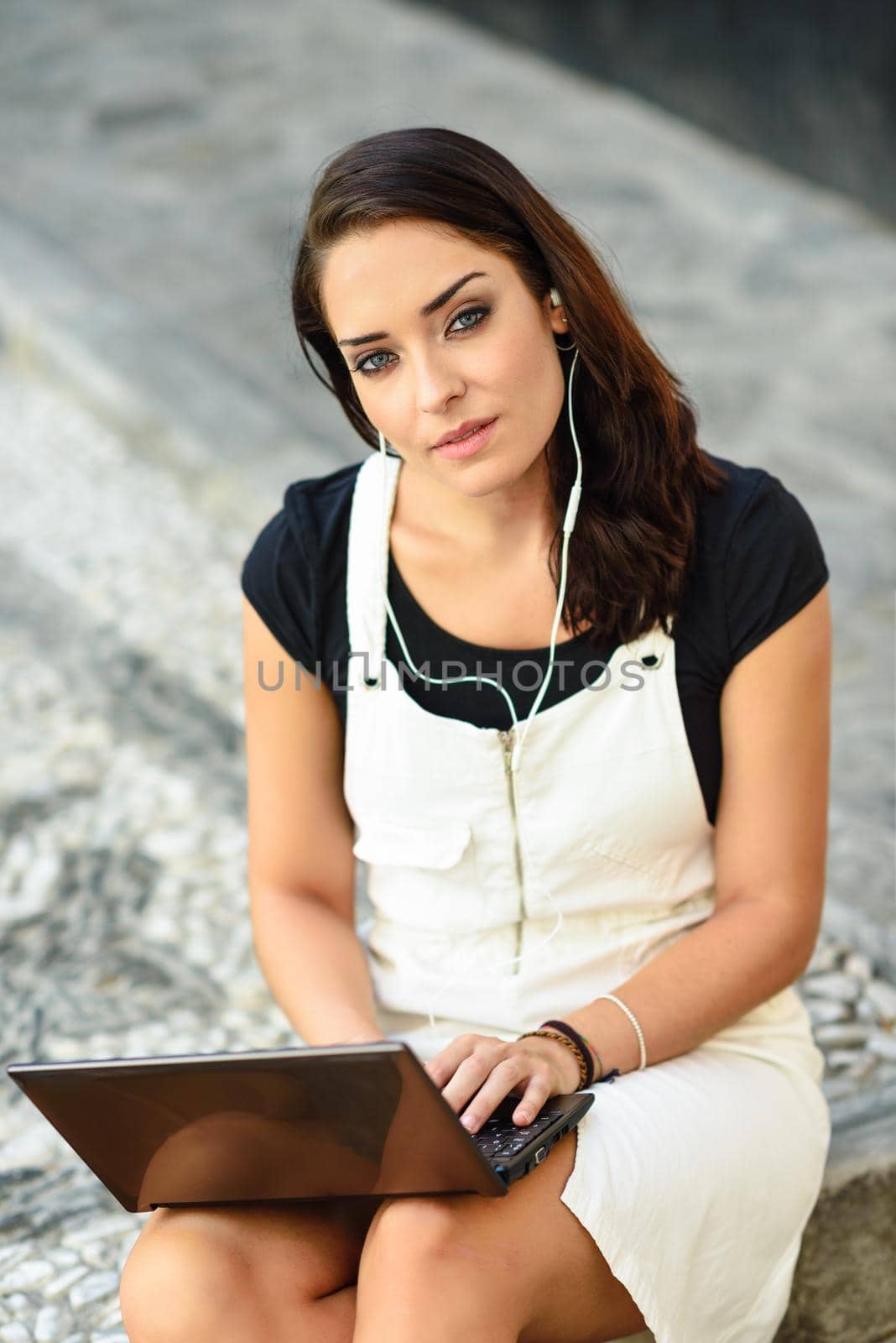 Beautiful young woman using laptop computer sitting on urban steps. Businesswoman wearing casual clothes working outdoors. Lifestyle concept.