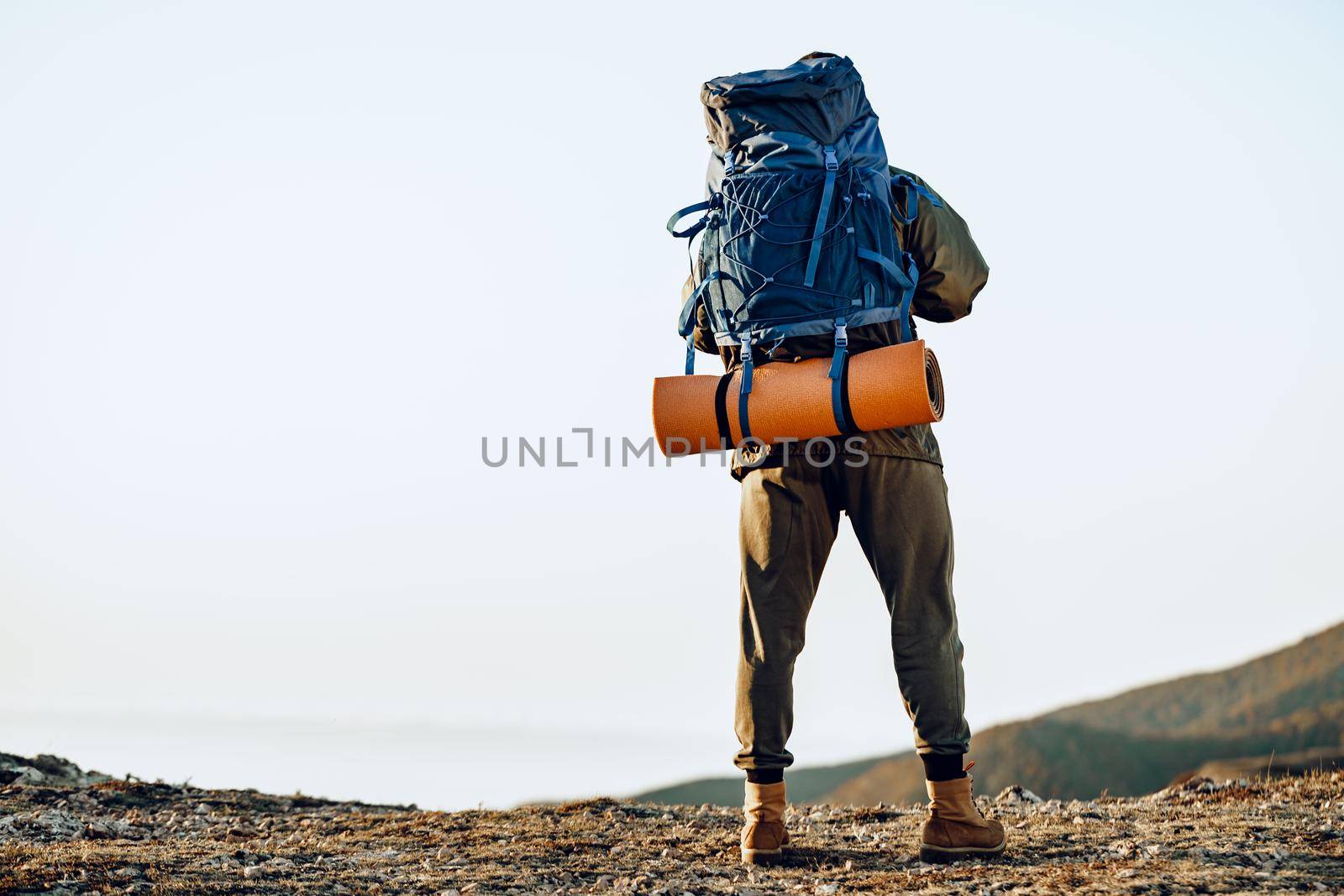 Unrecognizable man hiker got to the top of the mountain and looks down onto the valley