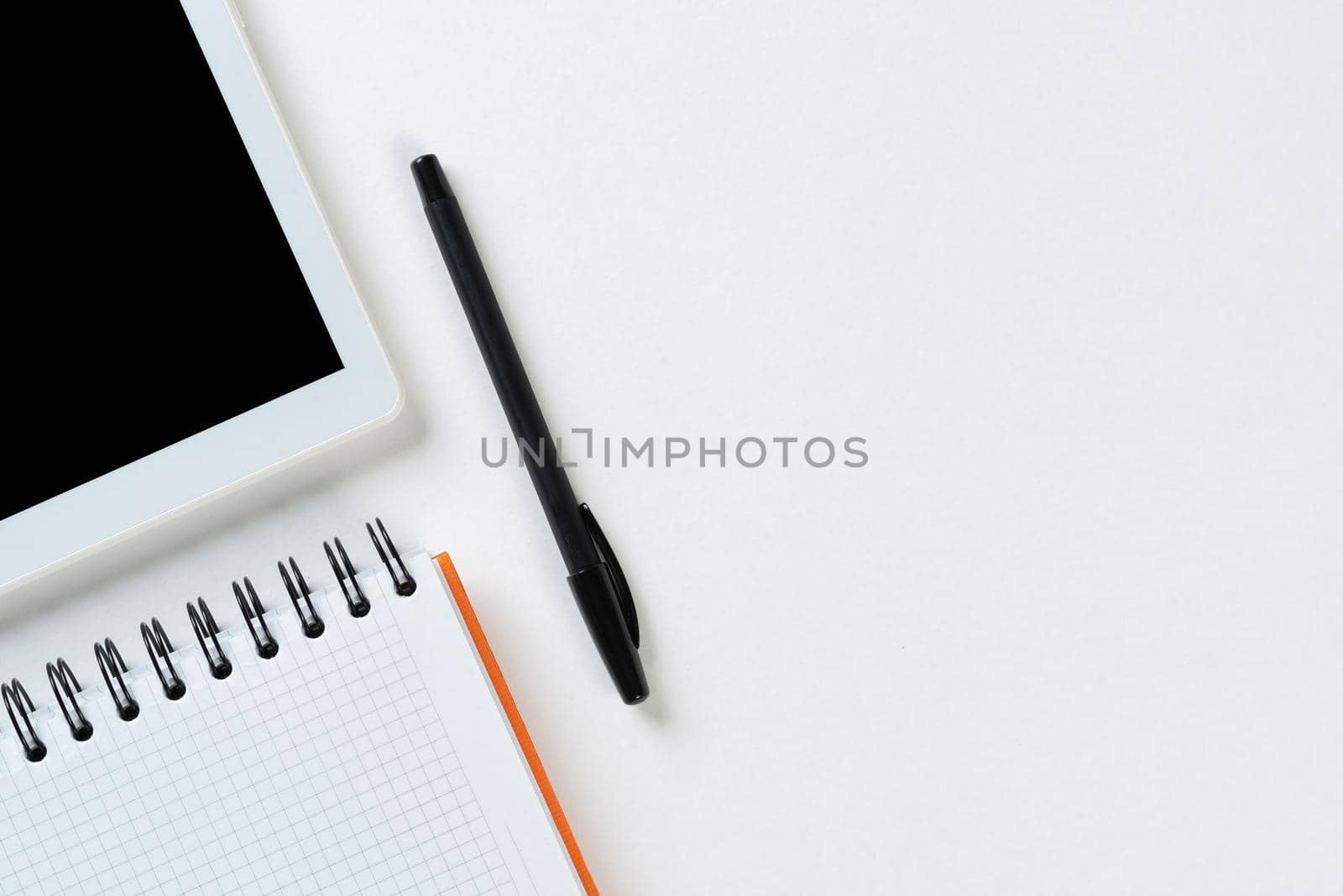 Top view of modern working place. Spiral notepad, pen and tablet computer on white surface. Education, creativity and innovation concept with copy space. Digital technology in modern business.