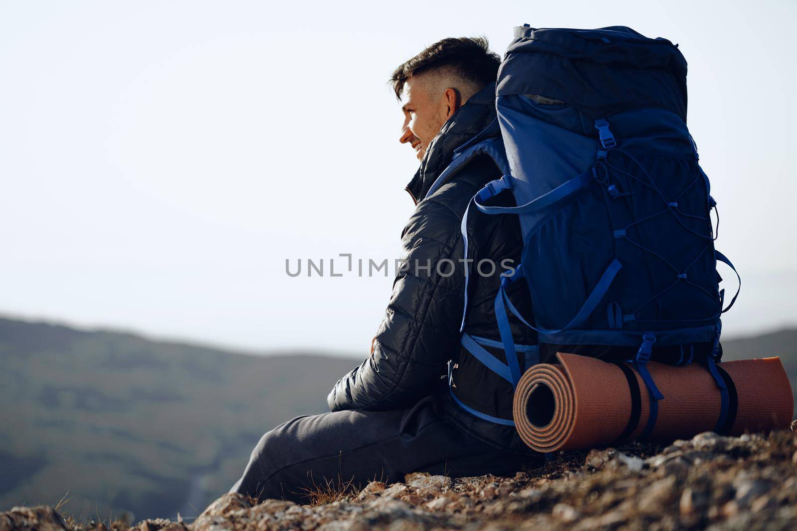 Young male hiker sitting and having a rest on a halt stop in mountains