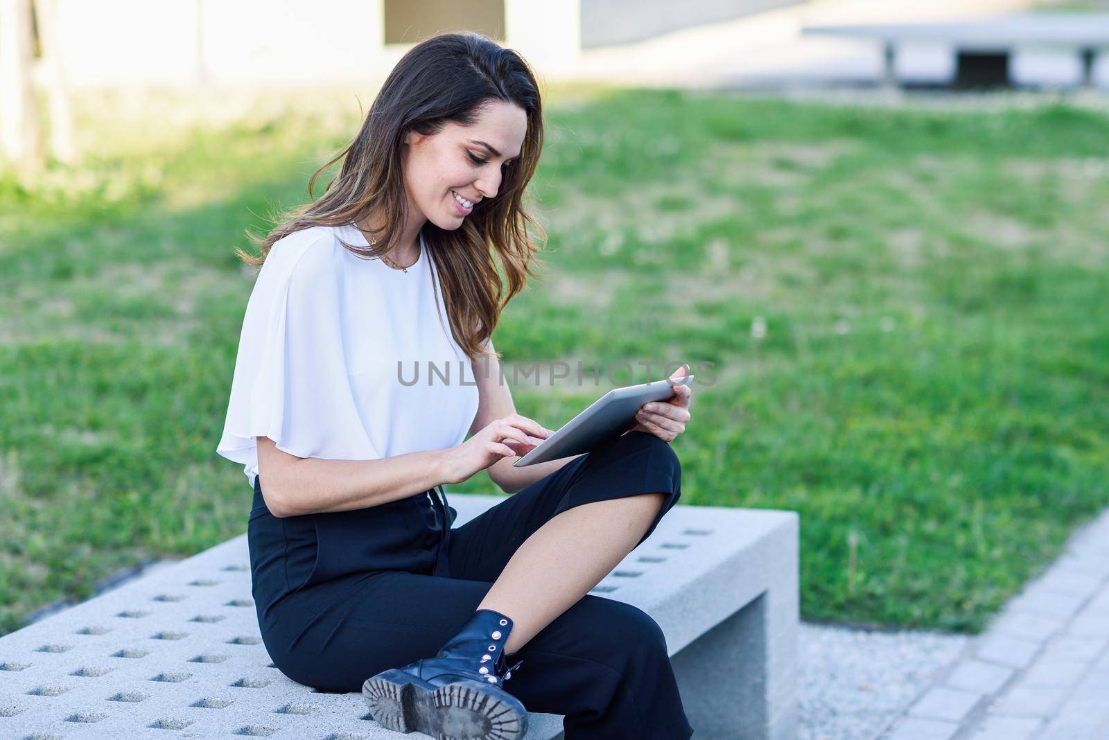 Middle-age woman using digital tablet sitting outdoors in urban background. by javiindy