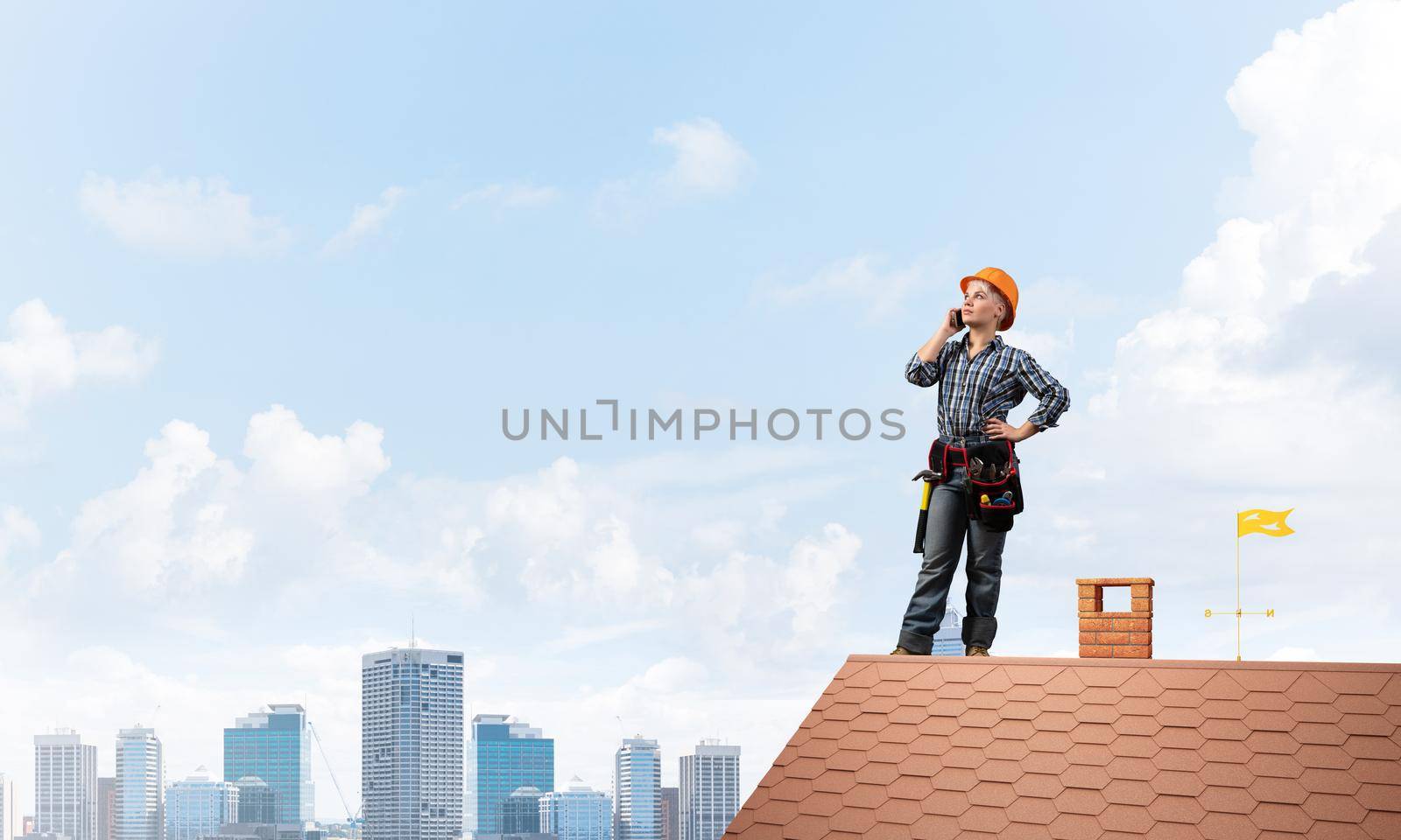 Attractive blonde woman in workwear and hardhat talking on smartphone. Young worker in checkered blue shirt standing on brick roof of building. Professional renovation and roofing construction.