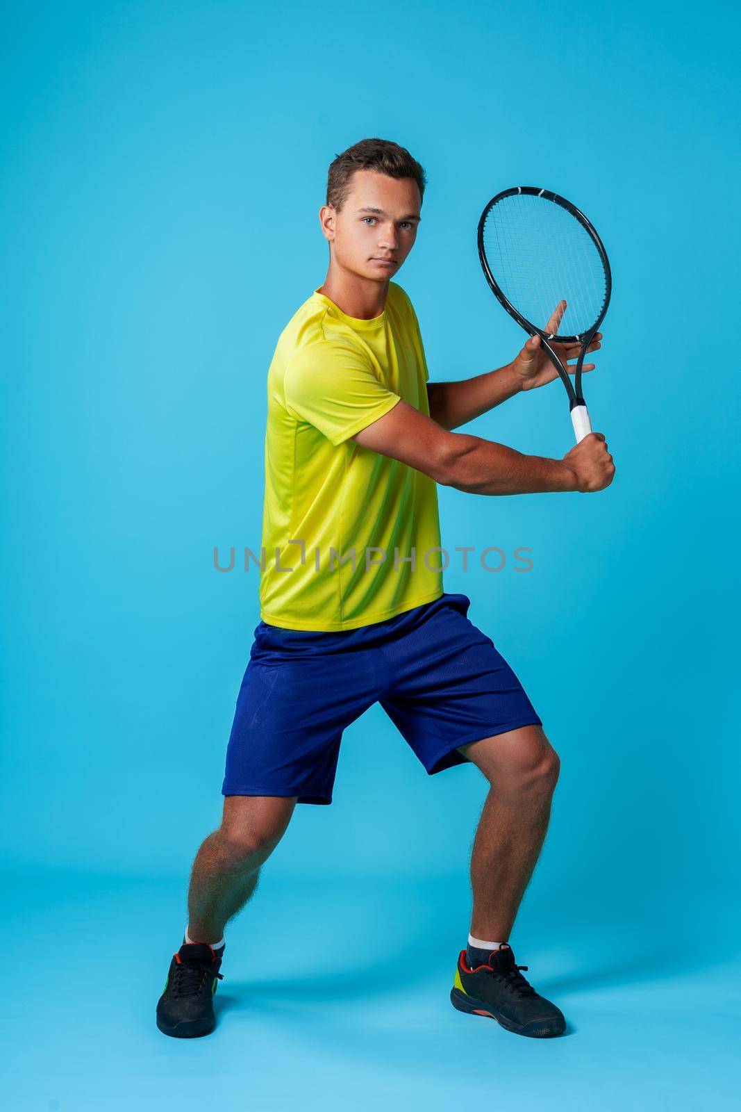 Full length studio portrait of a tennis player man on blue background close up