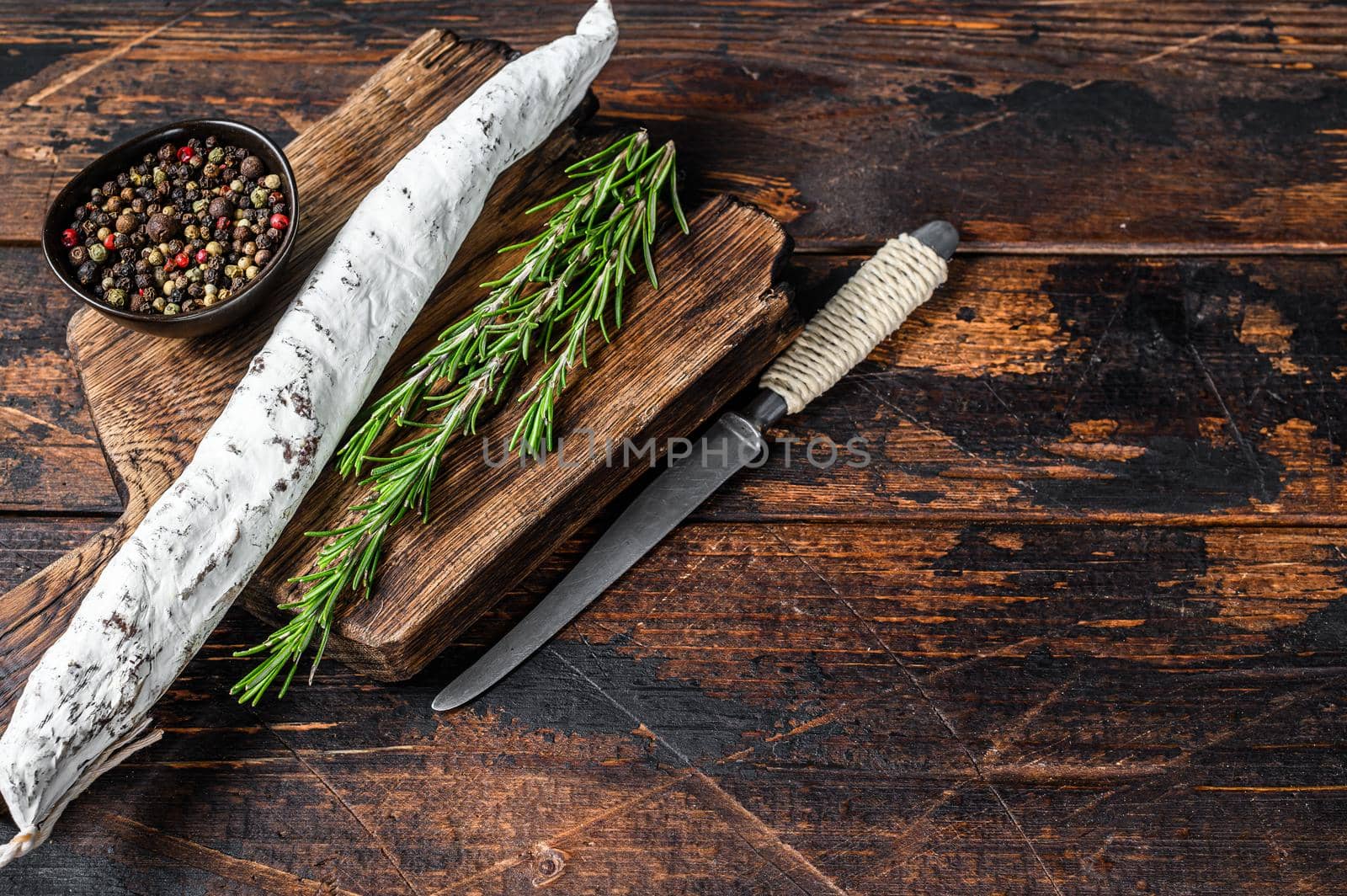 Spanish Fuet salami wurst on a wooden cutting board. Dark wooden background. Top view. Copy space.