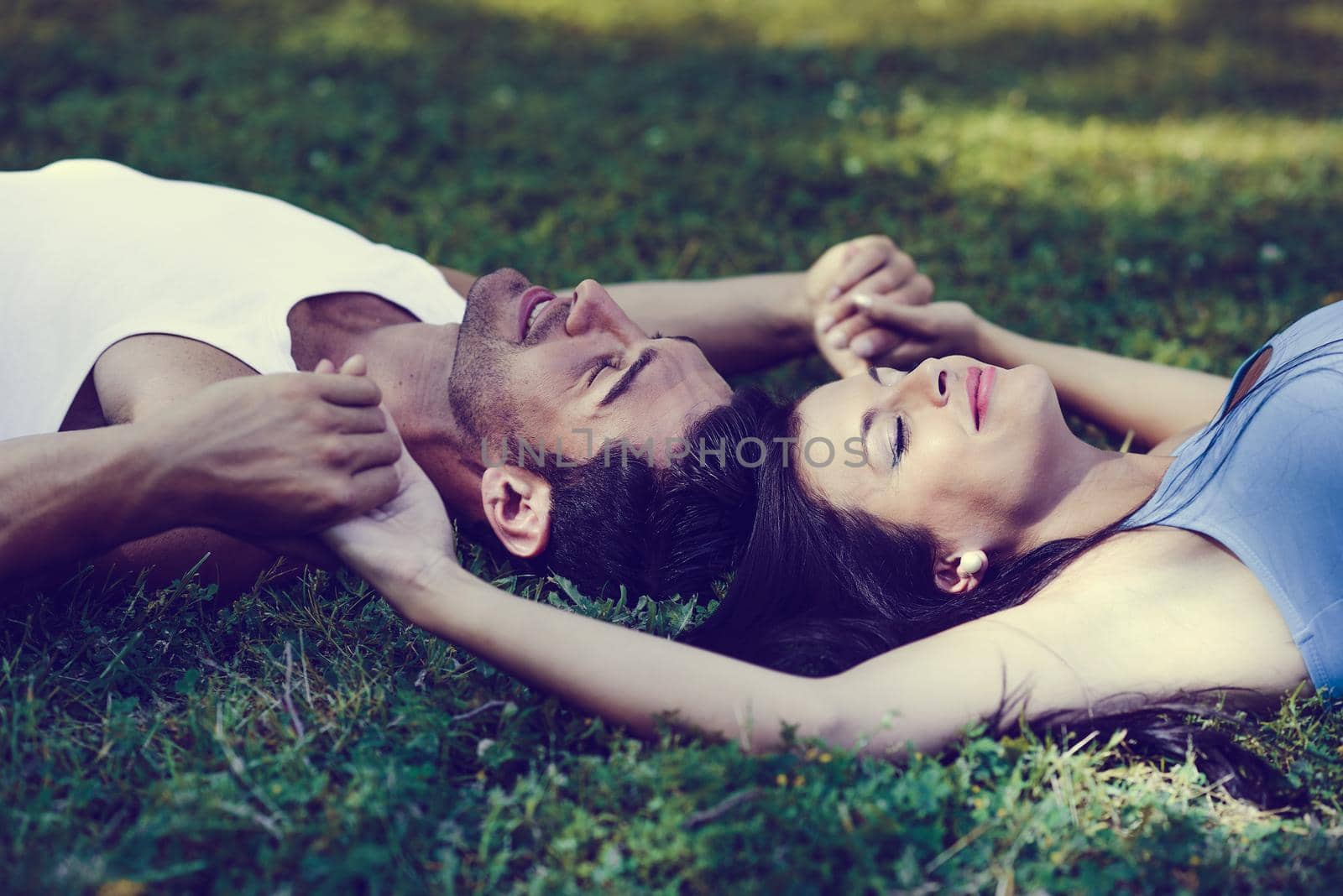 Happy smiling couple laying on green grass by javiindy