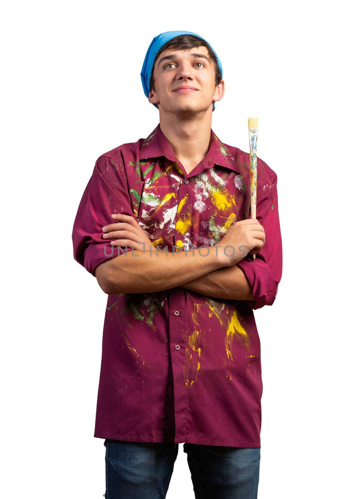 Smiling young painter artist holding paintbrush. Portrait of happy decorator looking upwards isolated on white background. Artistic occupation and creative profession. Art school student posing.