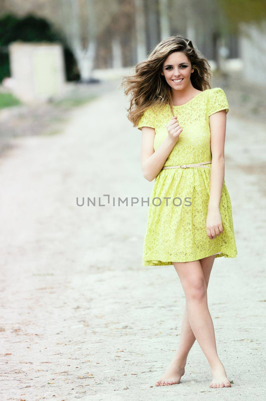 Beautiful blonde girl, dressed with a beige dress, standing in rural road