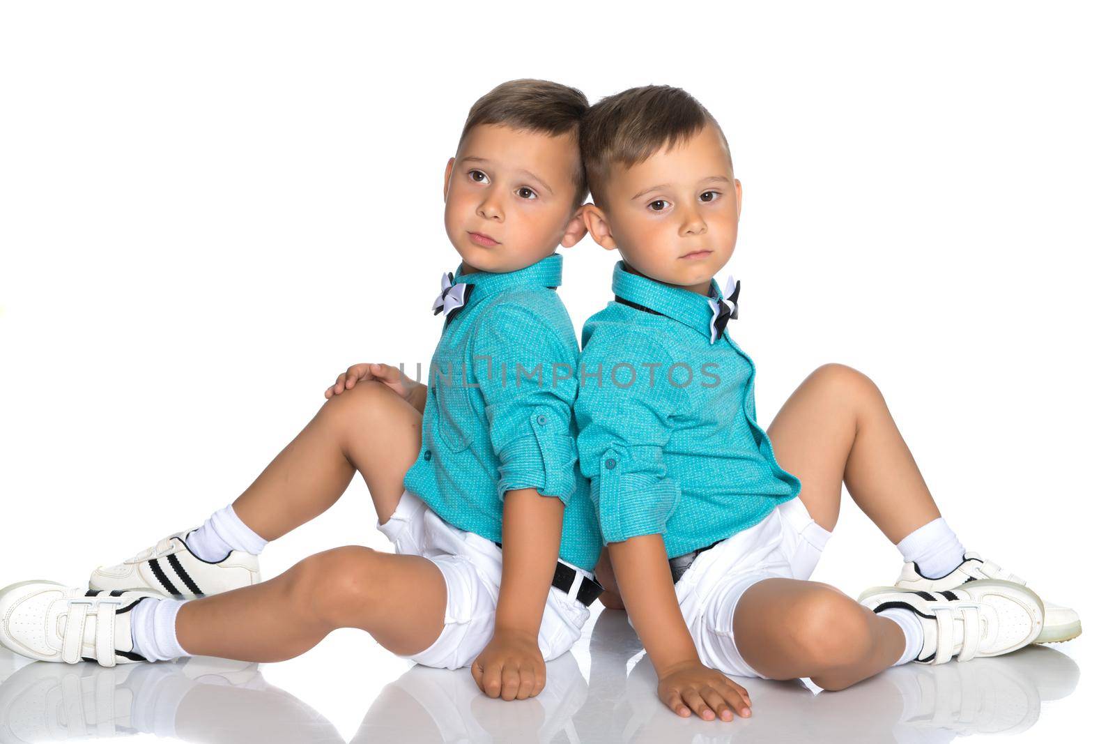 Two cute little boys, brothers sit on the floor in a studio on a white background. The concept of a happy childhood, the development of a child in the family. Isolated.
