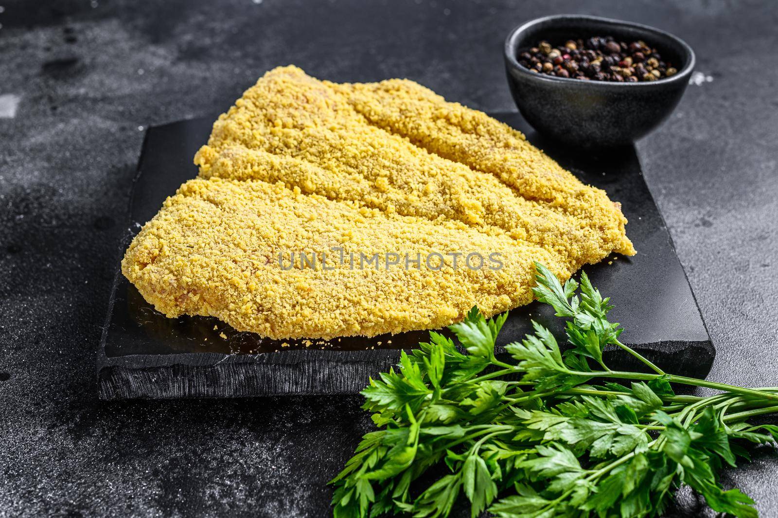 Raw large Viennese schnitzel on a cutting board. Black background. Top view.