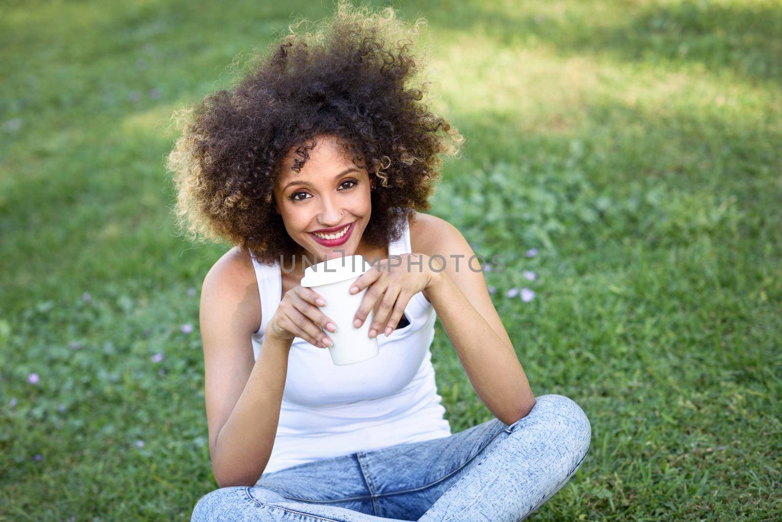 Woman with afro hairstyle drinking coffee in park by javiindy