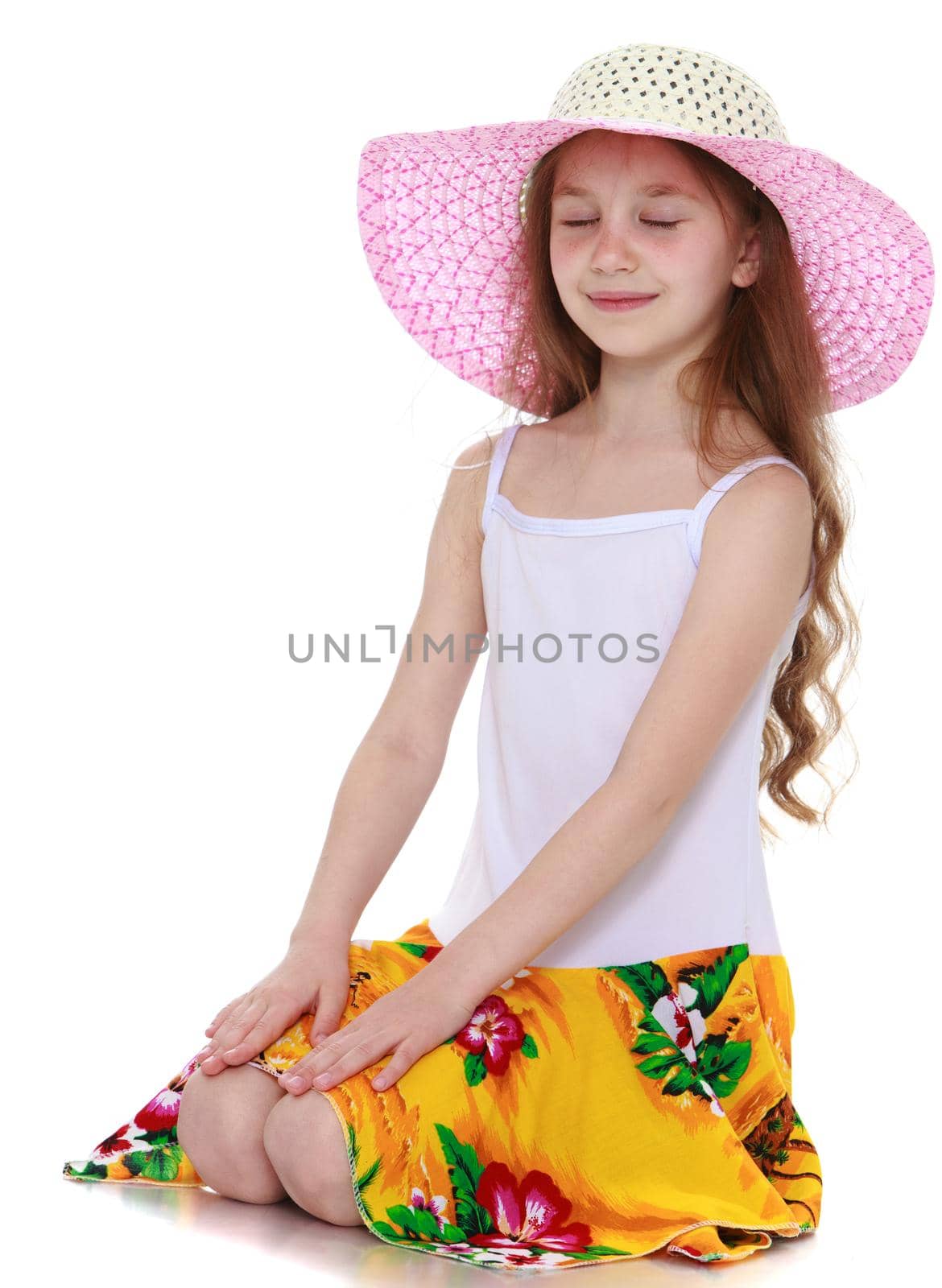 Nice little girl in a pink hat and a white tank top without a pattern . A girl stands on her knees closing her eyes , she engaged in meditation - Isolated on white background