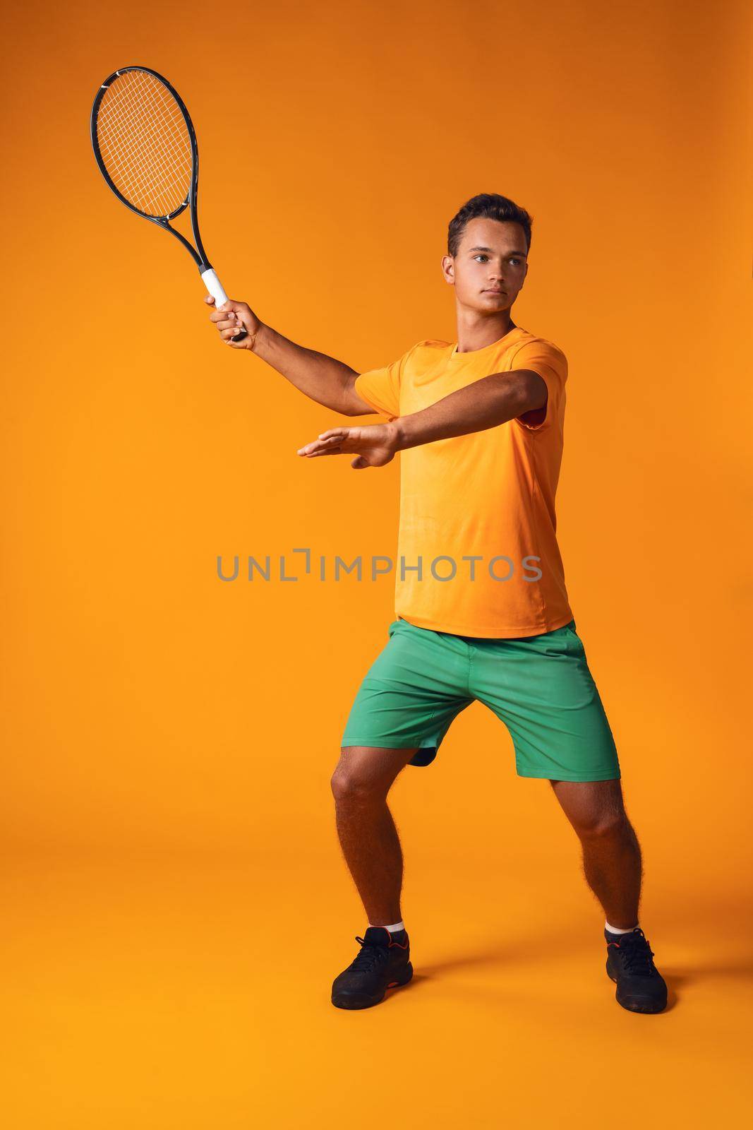 Full-length portrait of a tennis player man in action against orange background close up