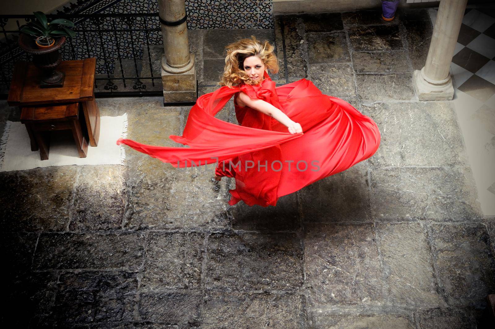 Portrait of a beautiful blonde woman, wearing a red dress, jumping