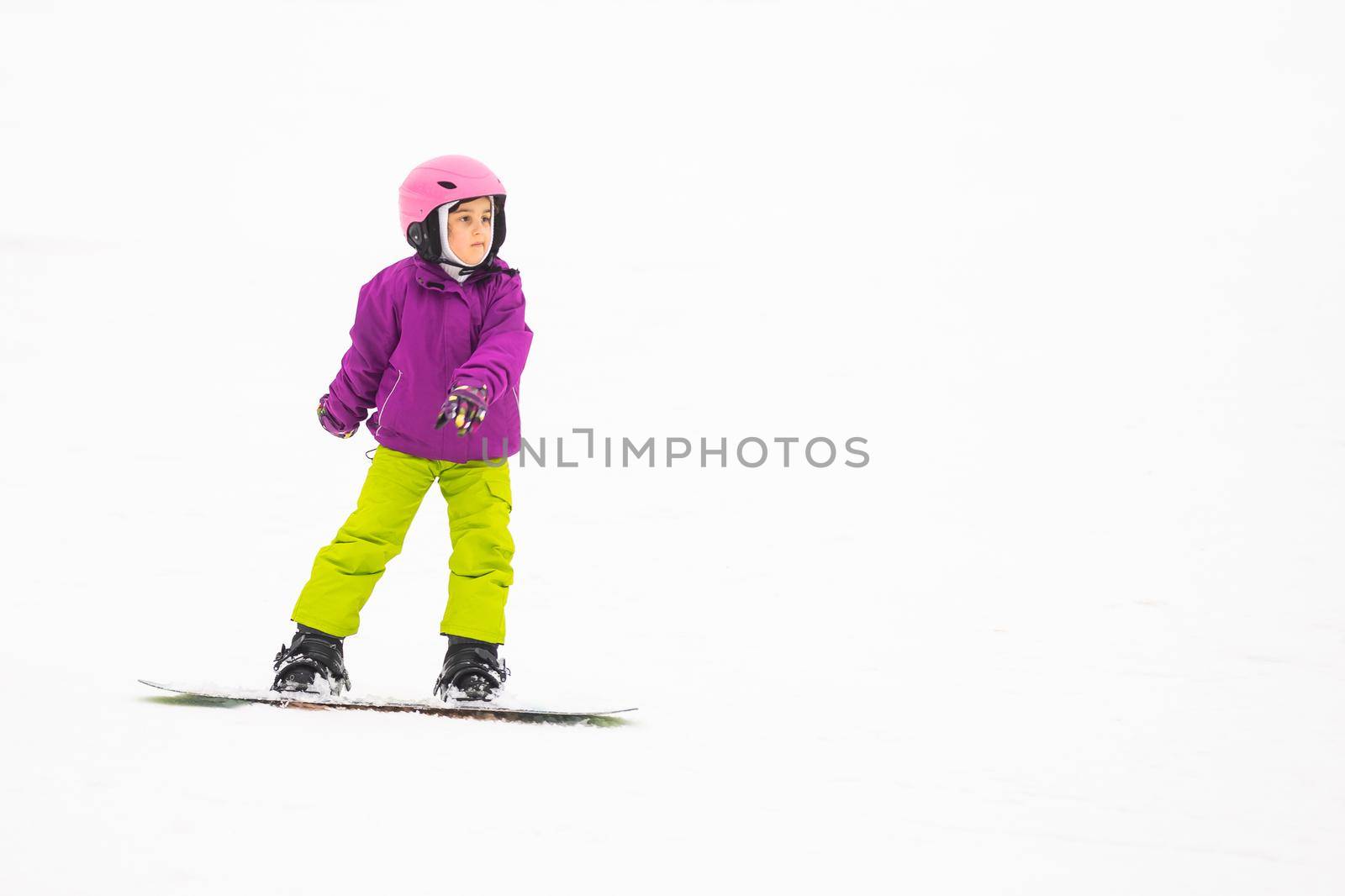 Snowboard Winter Sport. little girl learning to snowboard, wearing warm winter clothes. Winter background.