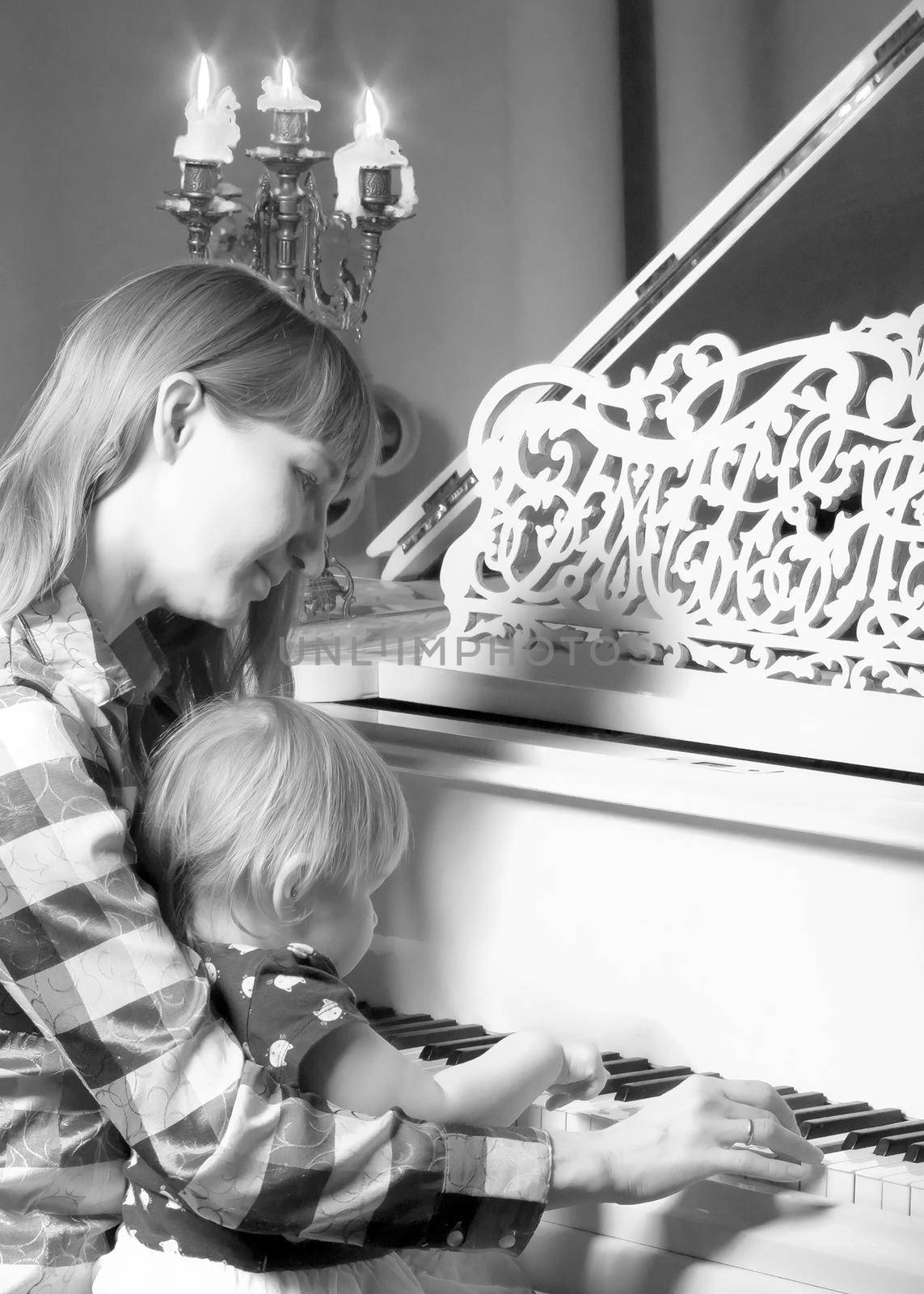 A young mother with a small child on Christmas night with candles near a large white piano. The concept of holidays and family happiness.