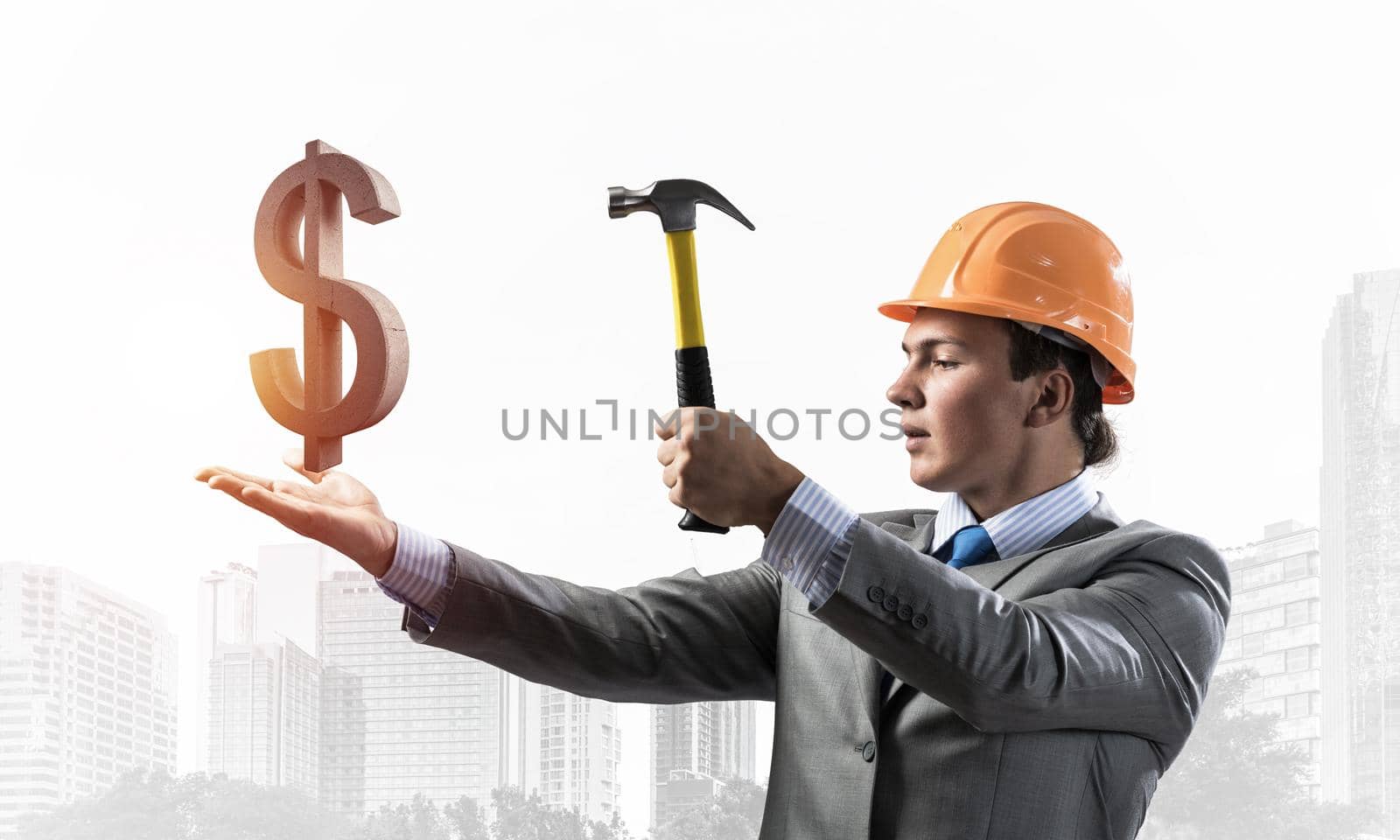 Businessman going to crash with hammer dollar sign. Young handsome man in business suit and safety helmet standing on cityscape background. Financial crisis, bankruptcy and inflation pressure.