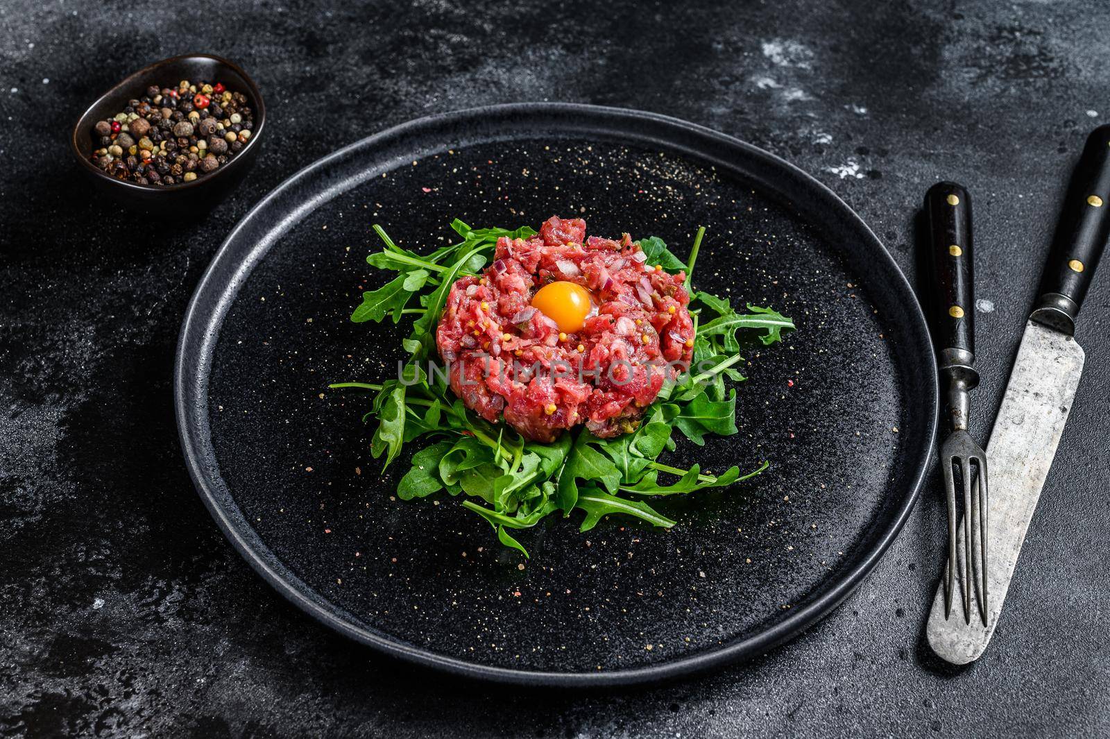 Beef tartar with a quail egg served on a black stone plate.. Black background. Top view.