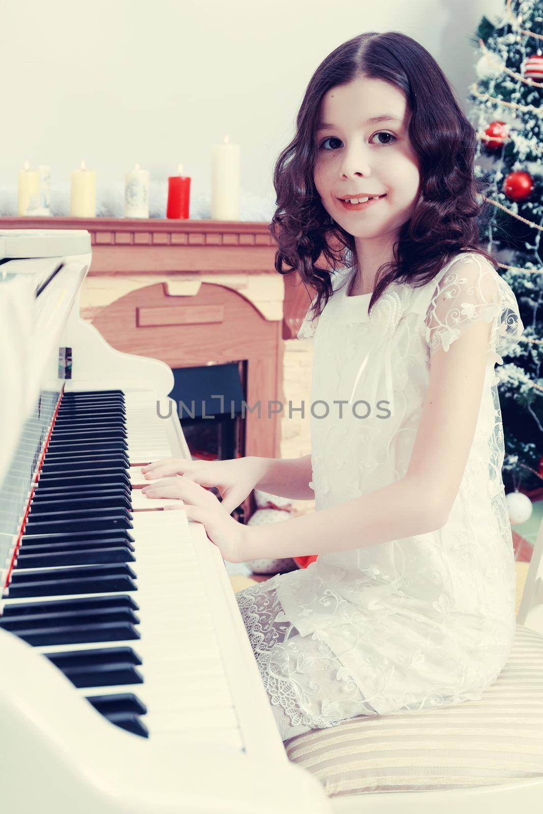 Adorable little girl new year's eve on the backdrop of the Christmas tree plays the piano.Creative toning of a photograph.