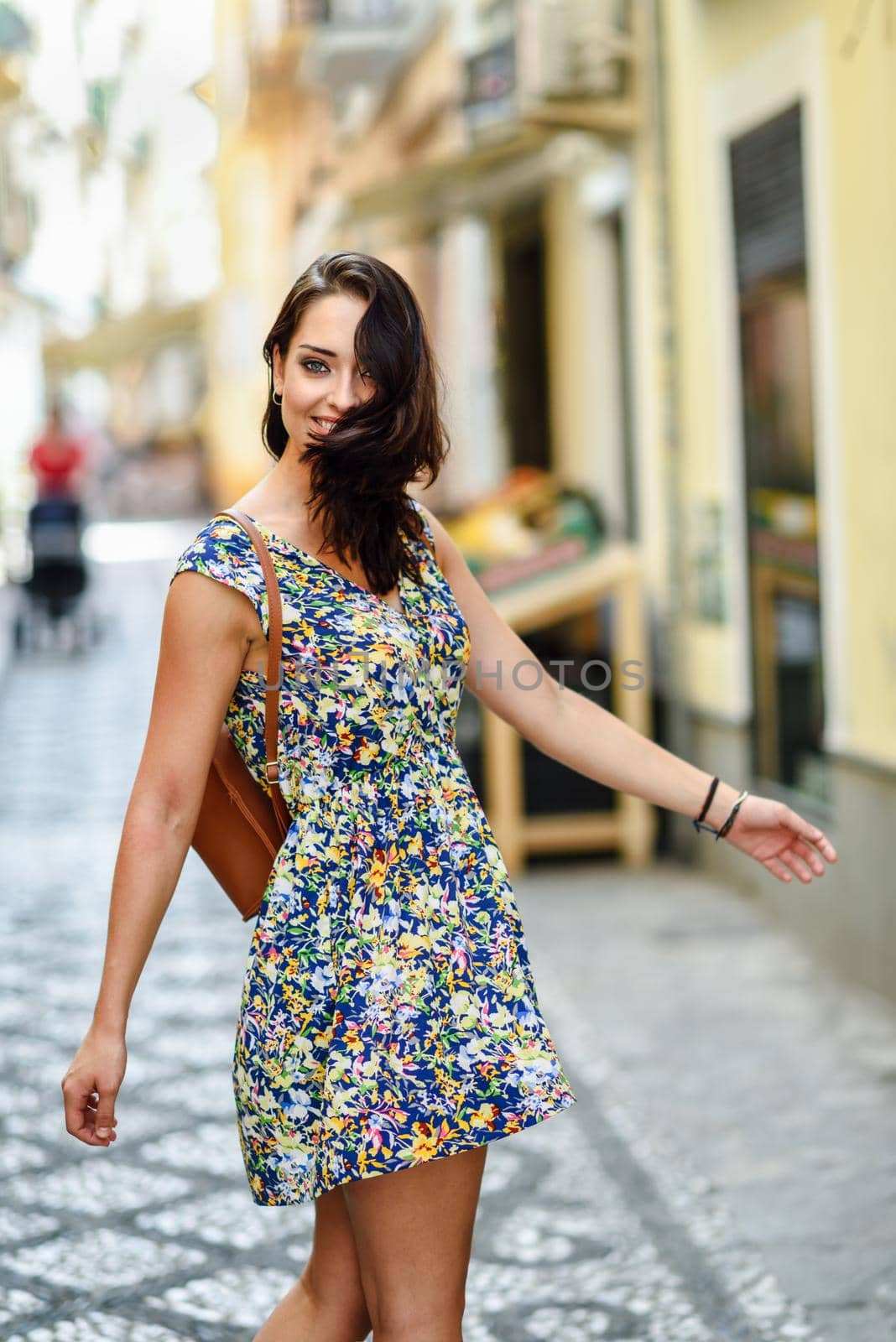 Happy young woman with blue eyes smiling outdoors. Girl wearing flower dress raising arms in urban background. Happiness concept.