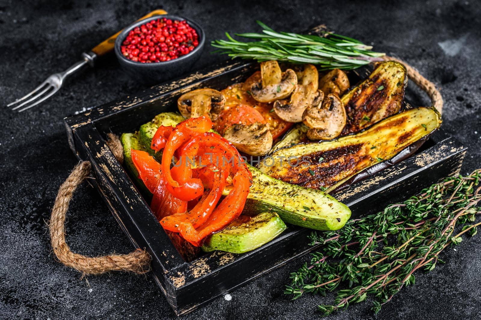 Baked vegetables bell pepper, zucchini, eggplant and tomato in a wooden tray. Black wooden background. Top view by Composter