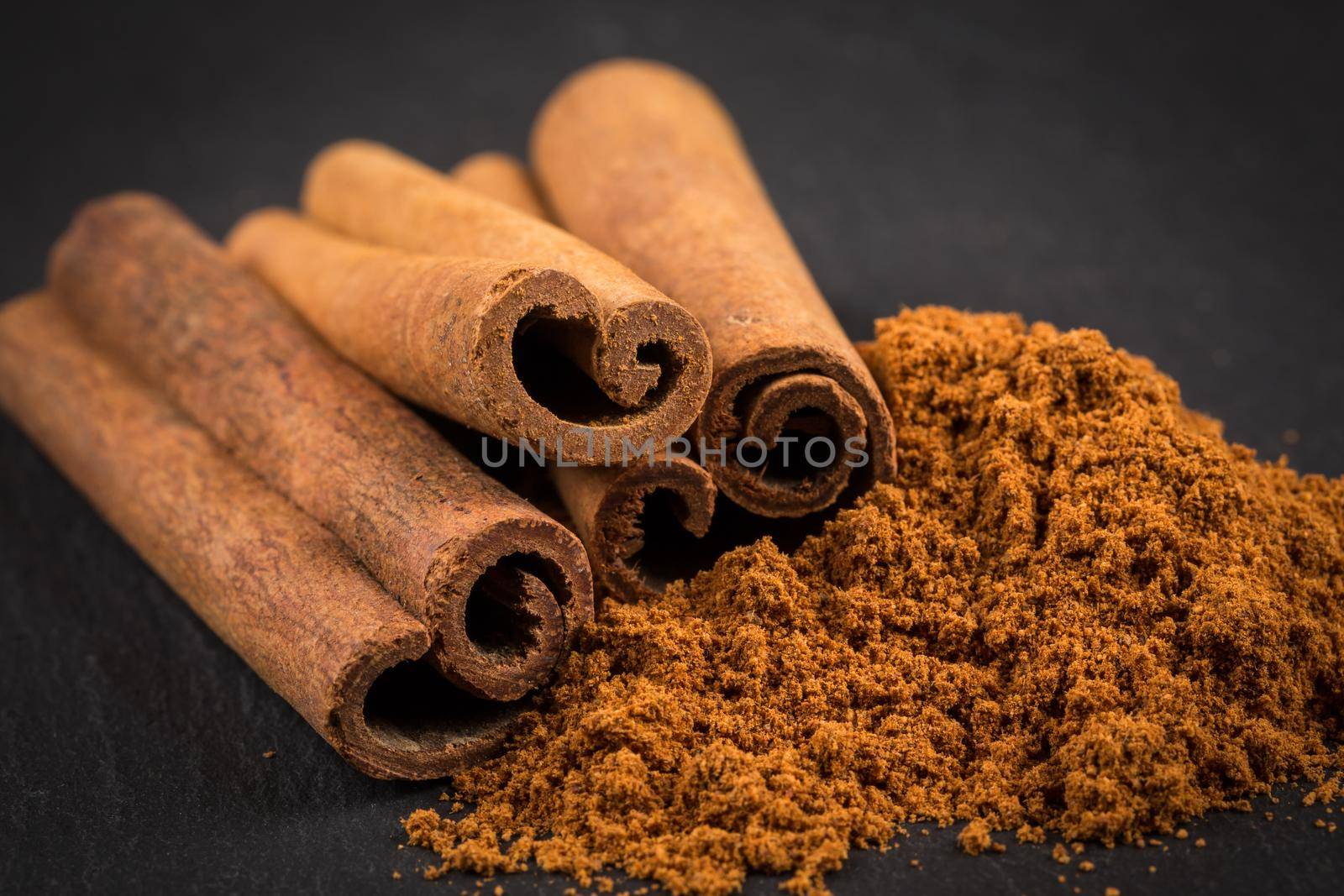 Cinnamon sticks with cinnamon powder on stone plate background