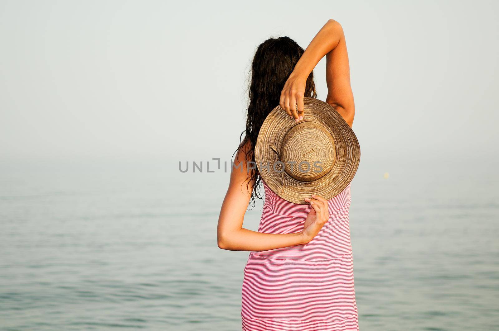 Portrait of a beautiful woman with long pink dress and sun hat on a tropical beach