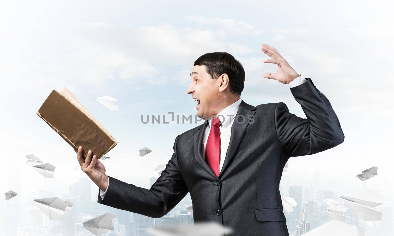 Expressive businessman holding open book. Emotional man in suit and tie standing on downtown background with flying paper planes. Excited manager shouting into book. Professional reference information