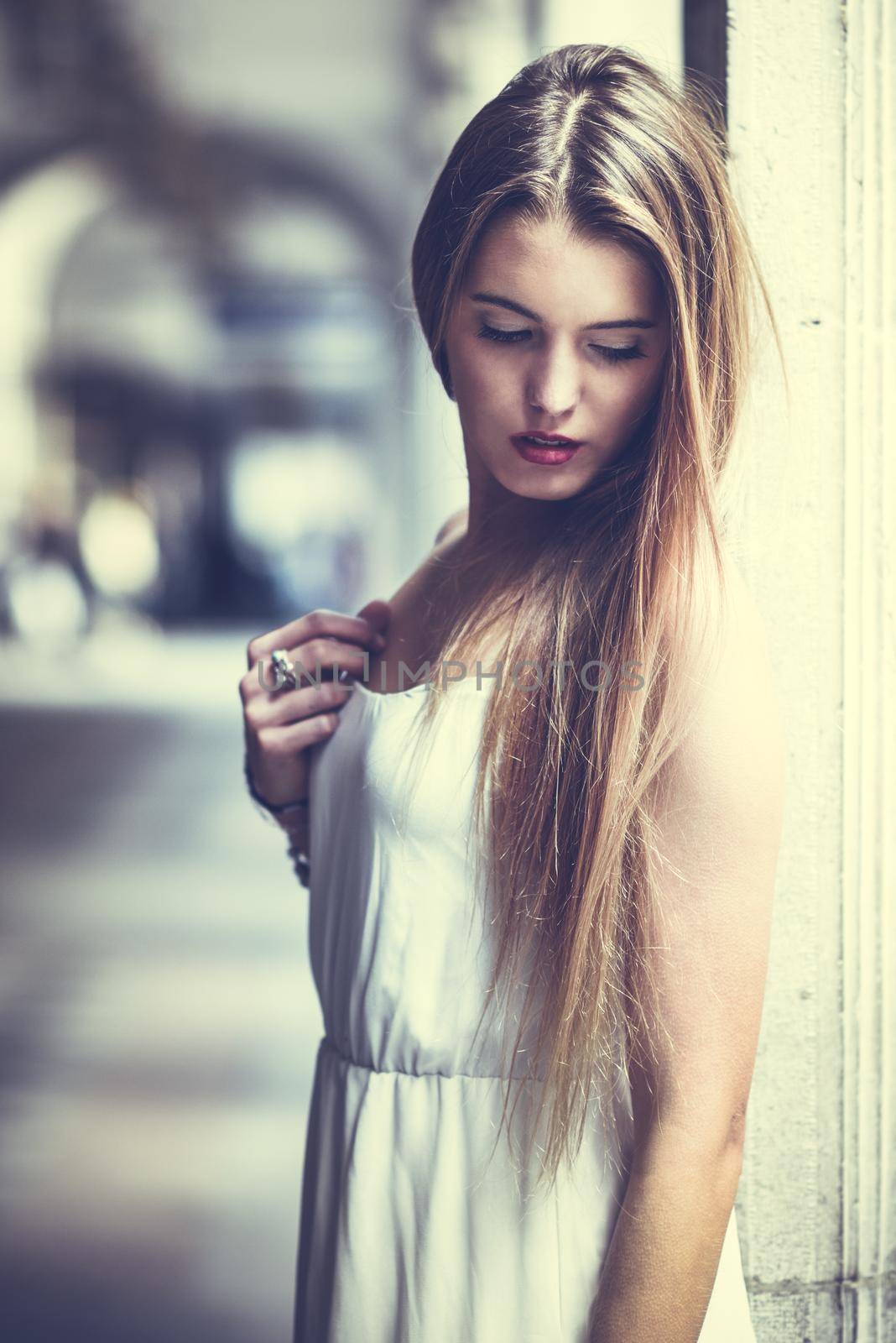 Portrait of beautiful blonde girl in urban background wearing white dress in urban background