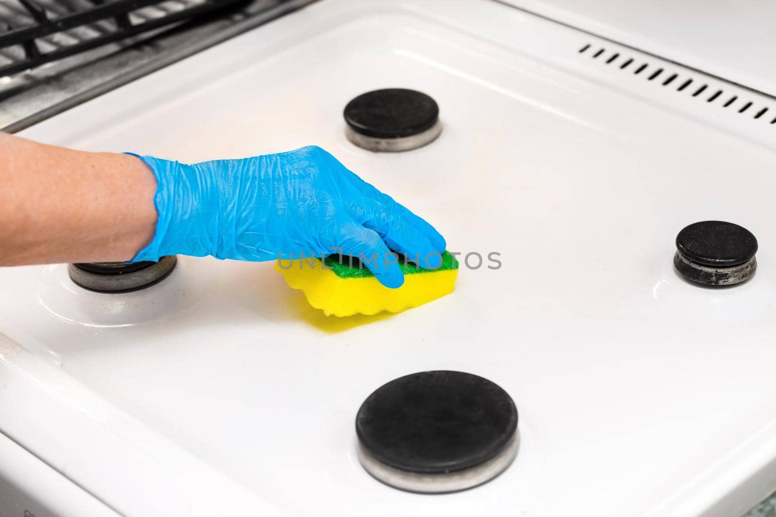 Woman's hand in a household glove sponges a gas stove. Cleaning the kitchen and washing the burners.