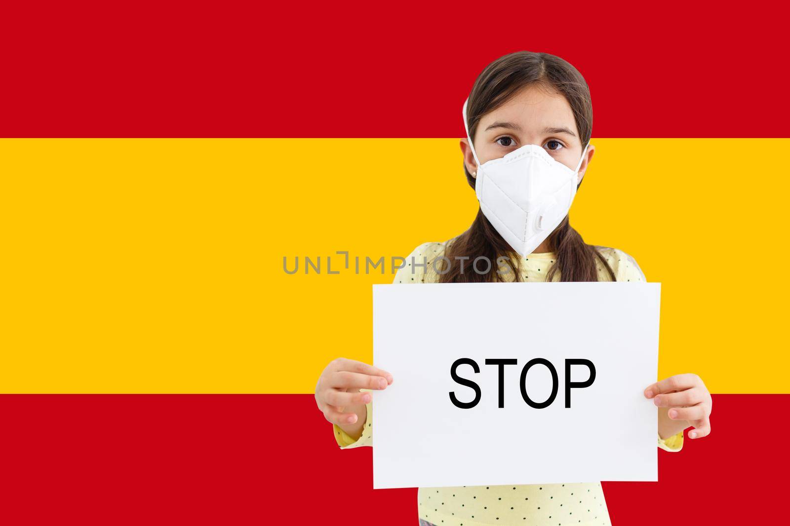 Masked little girl looking at the camera on flag Spain background. The concept of attention to the worldwide spread of the coronavirus worldwide. Coronavirus, virus in Spain.