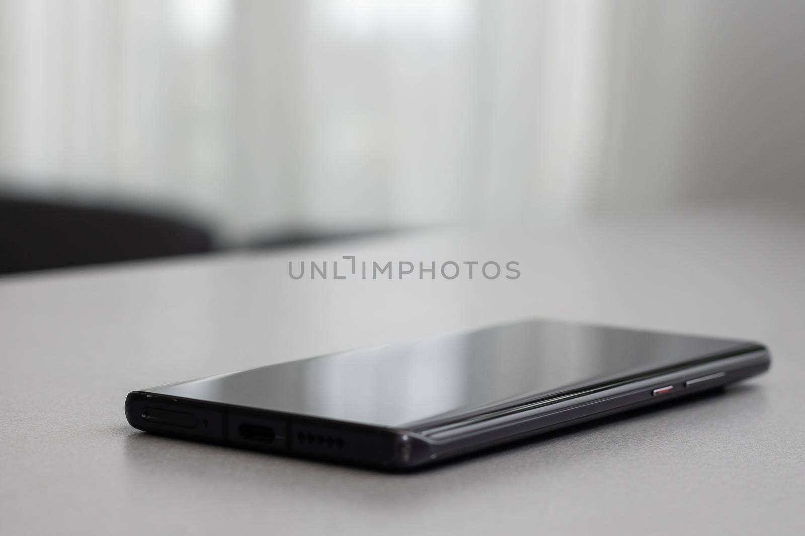 Black modern mobile phone with blank screen on black stone table background. Smartphone on old dark grey vintage texture background.