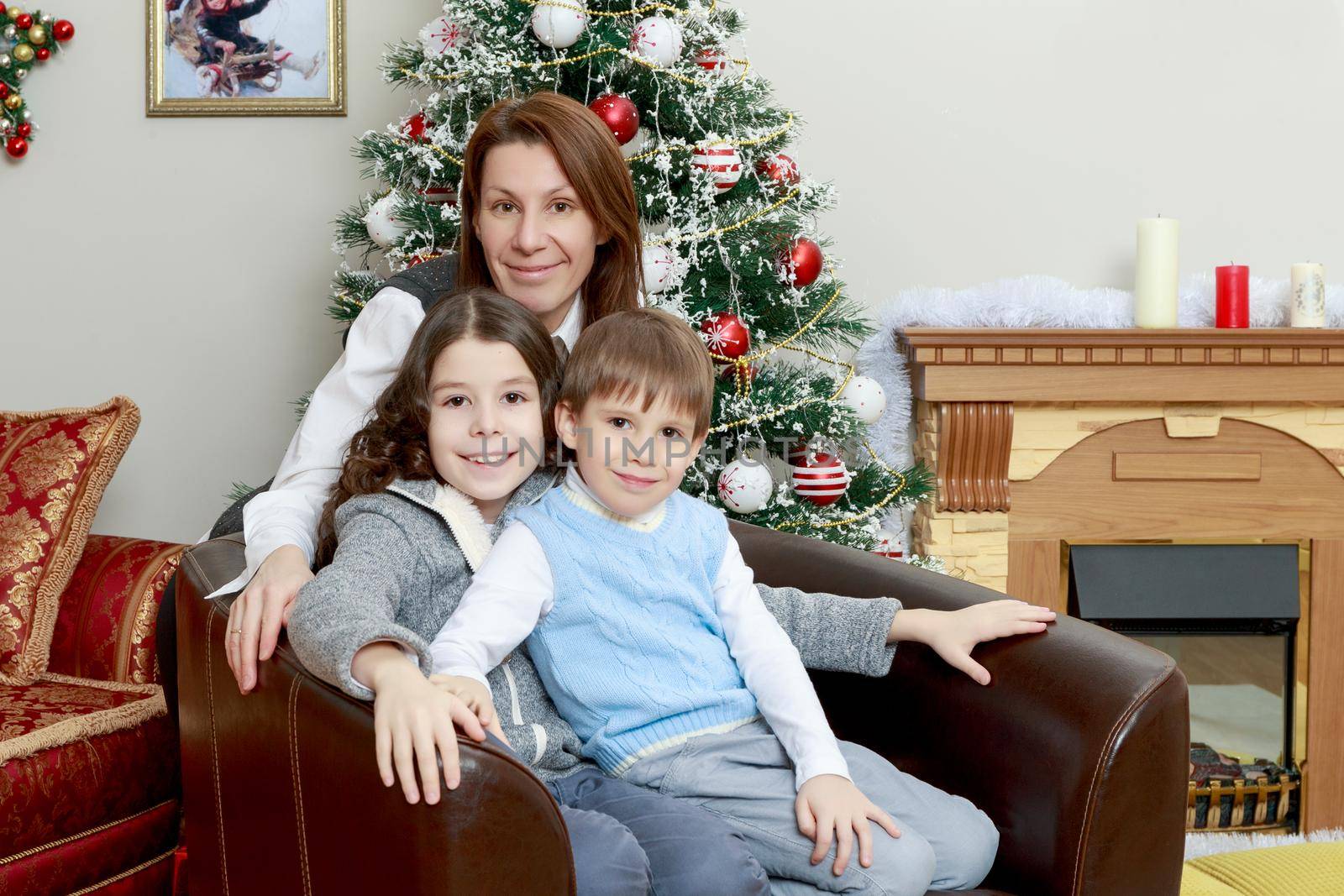 Happy mother hug her beloved children, daughter and son. On the couch by the Christmas tree.