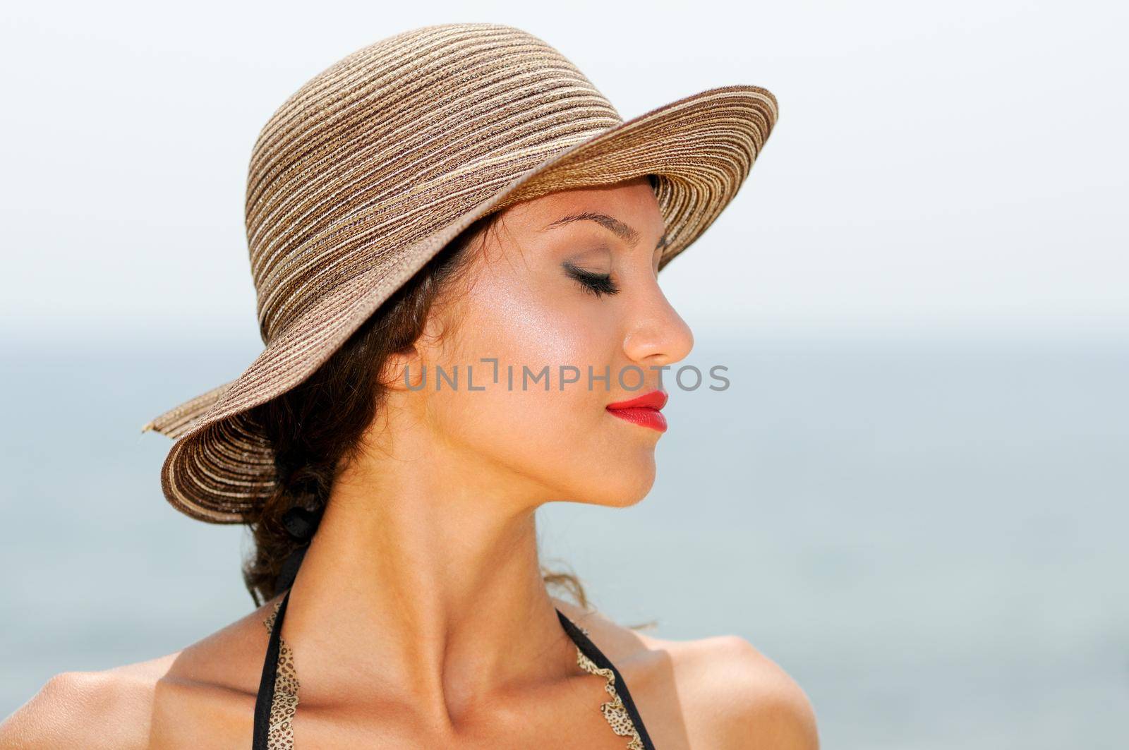 Close up portrait of an beautiful woman wearing sun hat on a tropical beach with her eyes closed