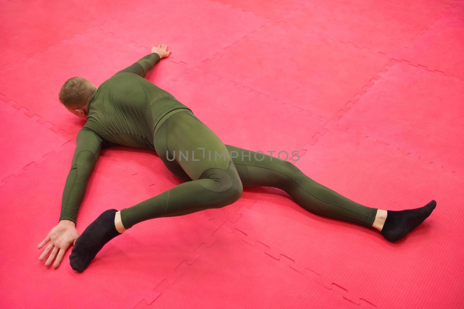 Young sports guy in a green thermal suit does exercises on the gym floor.