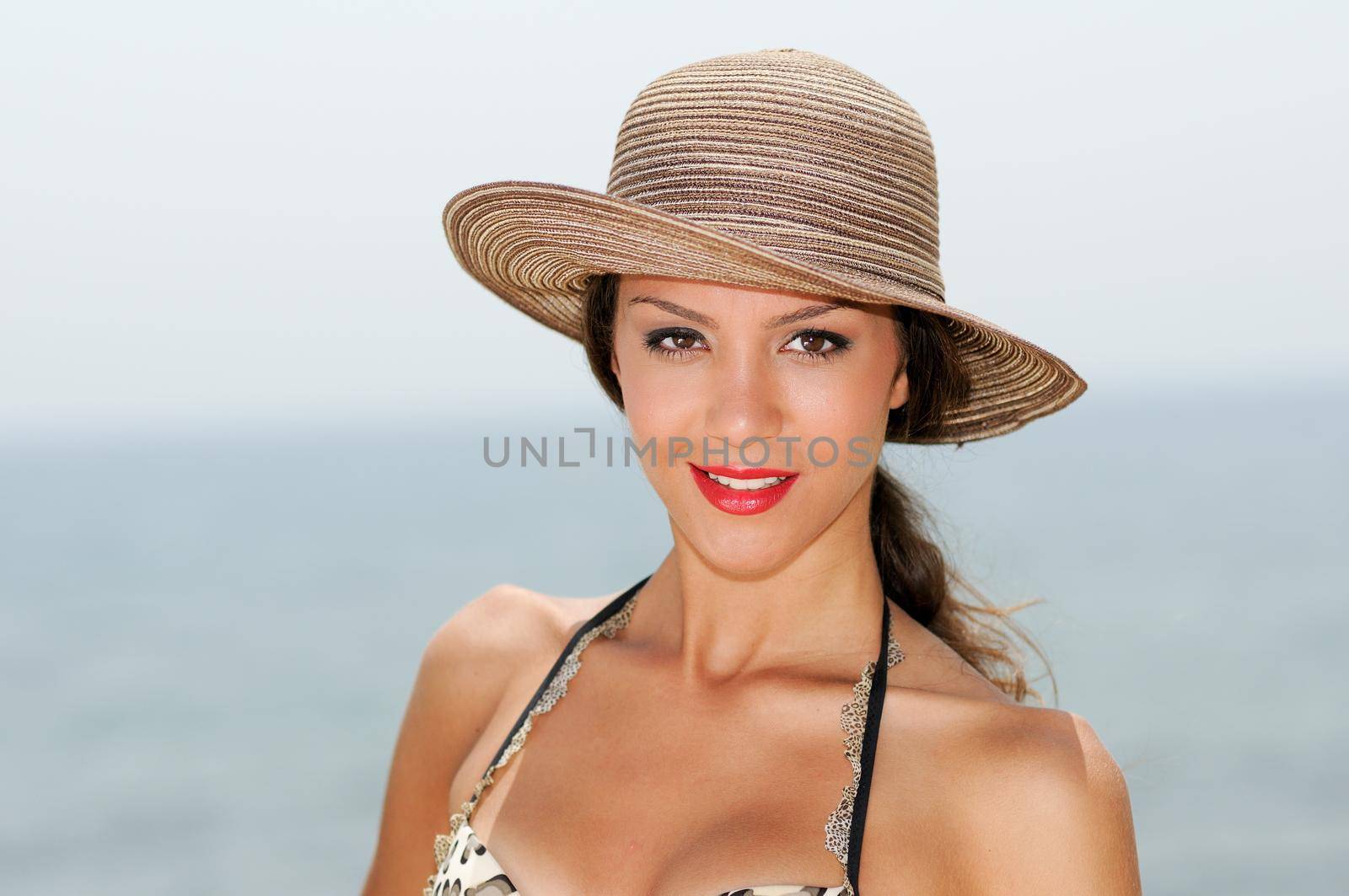 Close up portrait of an beautiful woman smiling with a sun hat on a tropical beach