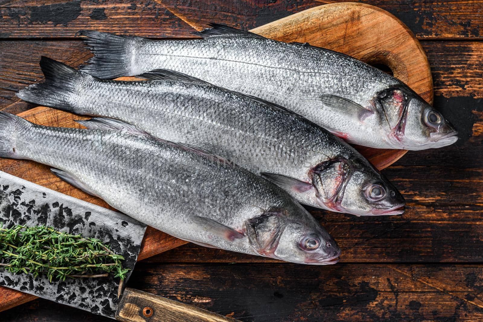 Fresh raw fish seabass on a cutting board. Dark wooden background. Top view.