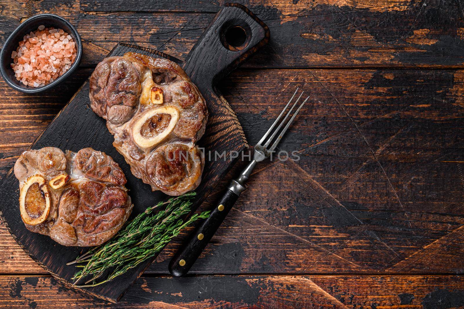 Stewed meat on the bone Osso Buco beef shank, italian ossobuco steak. Dark wooden background. Top view. Copy space by Composter