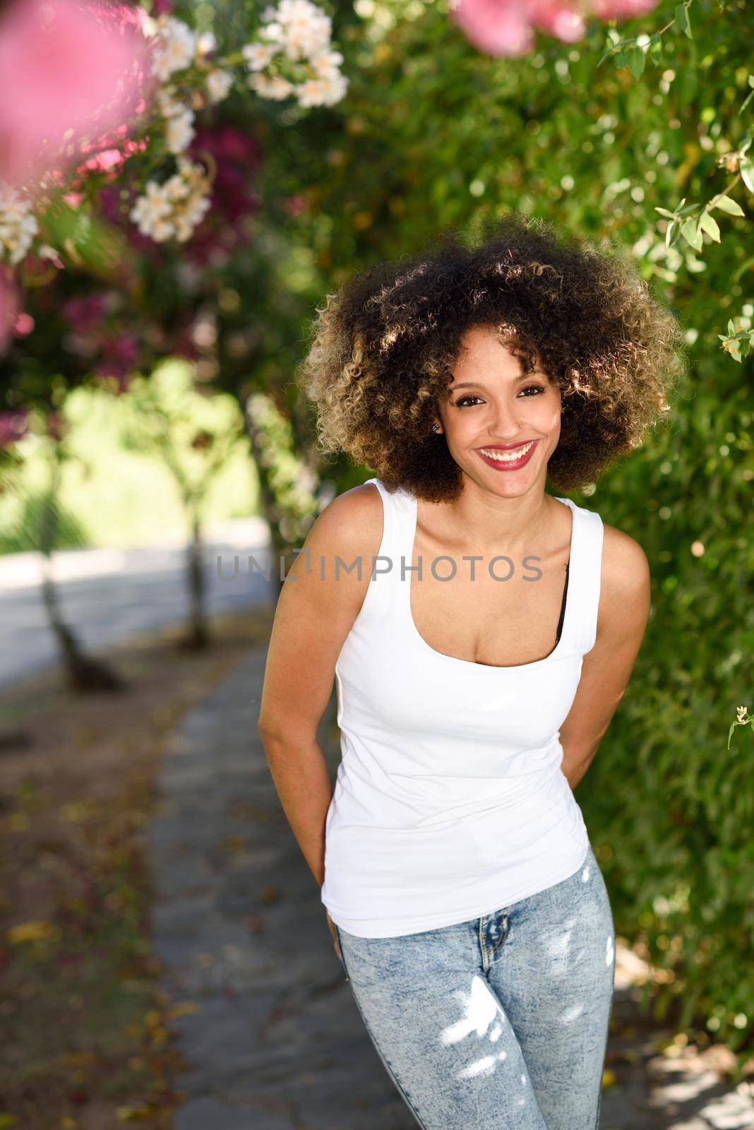 Young black woman with afro hairstyle smiling in urban park. Mixed girl wearing casual clothes.