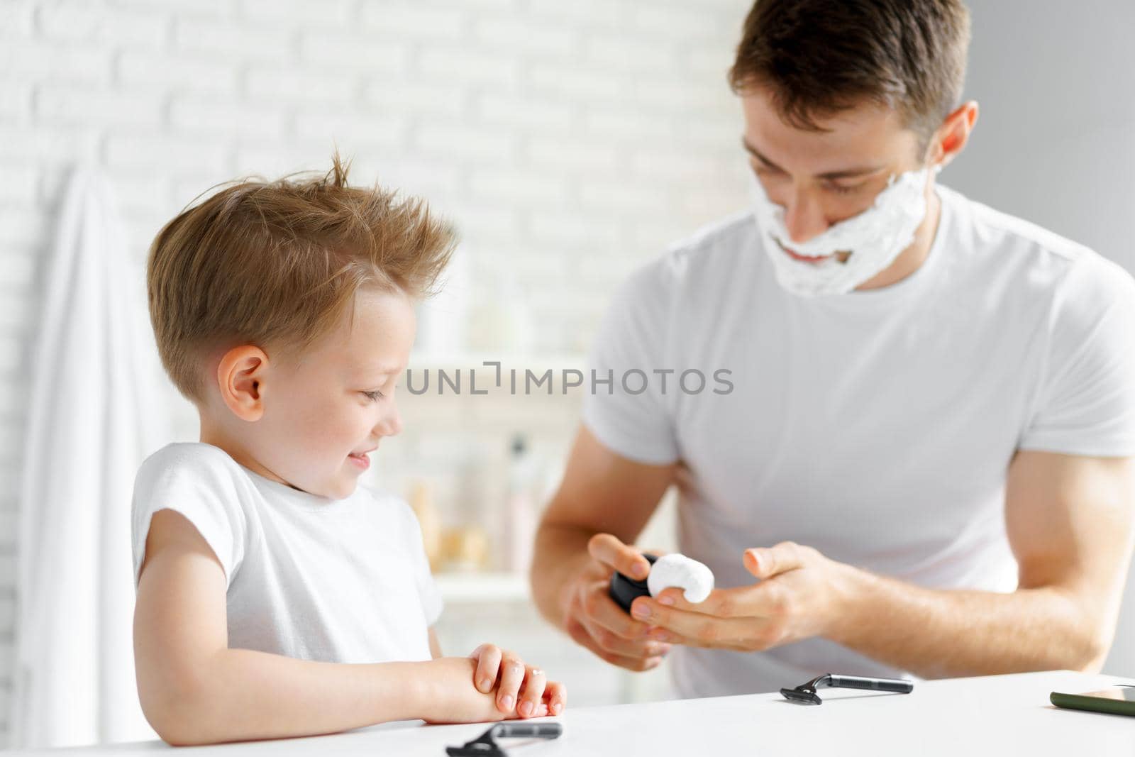 Father teaches his little son how to shave face in bathroom