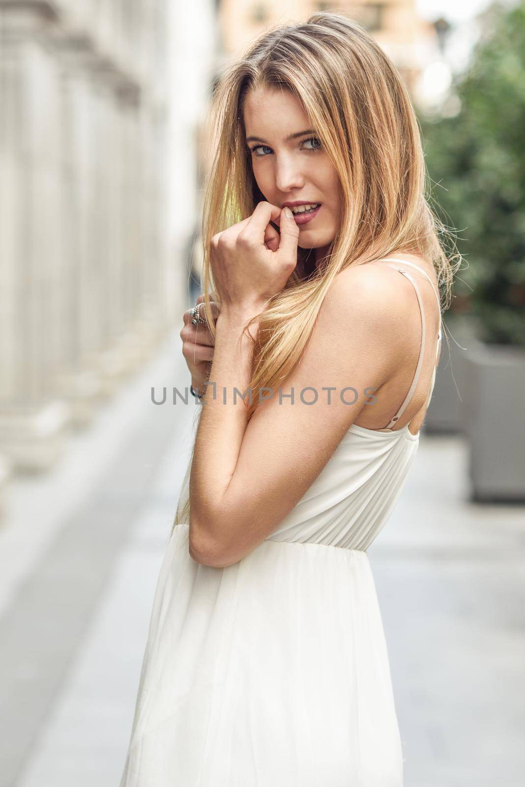 Portrait of beautiful blonde girl in urban background wearing white dress