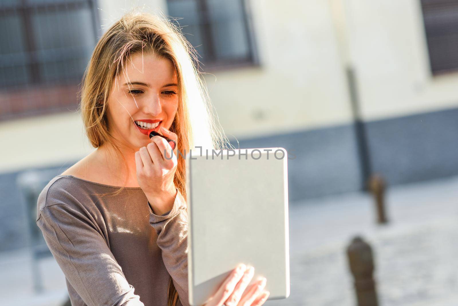 Young woman applying lipstick looking at tablet by javiindy