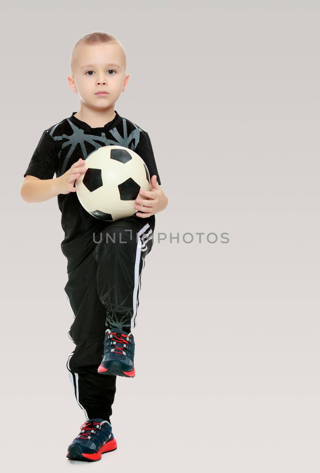 Cute little boy with the ball.He produces the ball with his knee.On a gray background.
