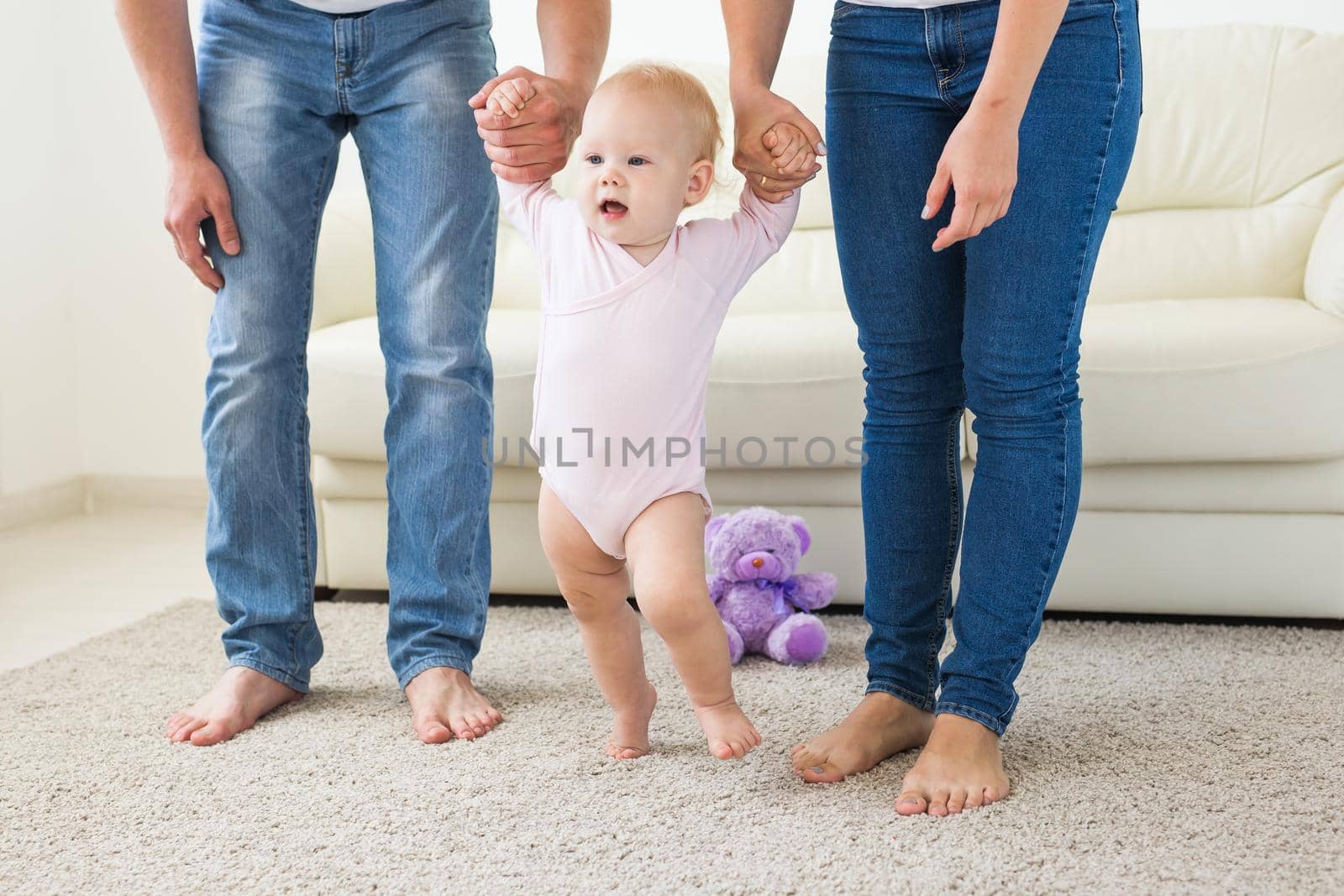 Baby taking first steps with mother's and father's help at home.