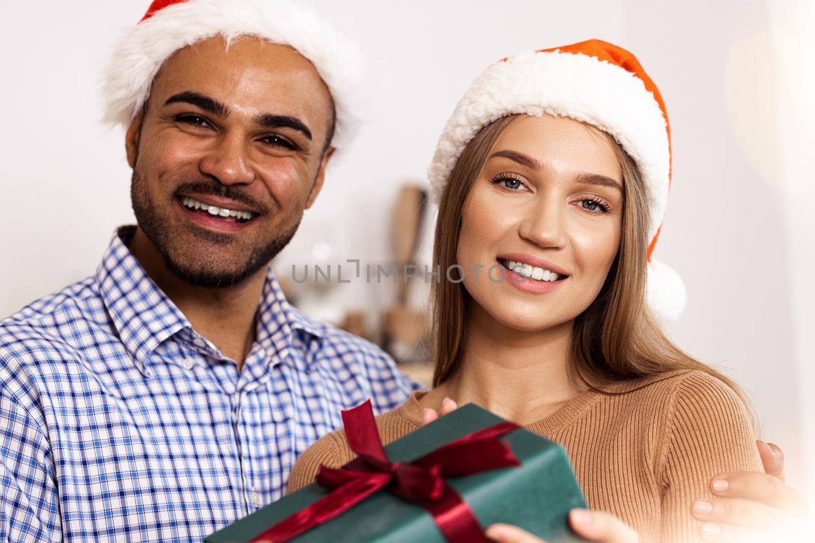 Romantic multiethnic couple in Christmas hats exchanging gifts, close up portrait