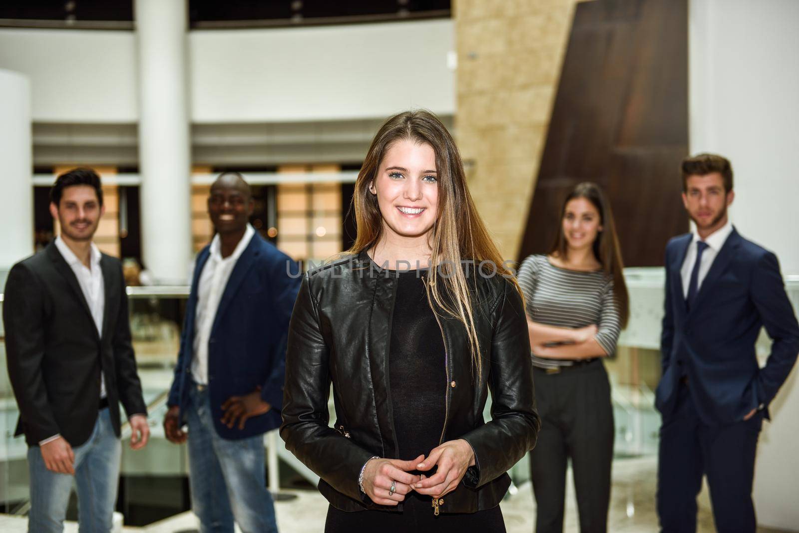 Blonde businesswoman leader looking at camera in office building. Group of multi-ethnic people in the background