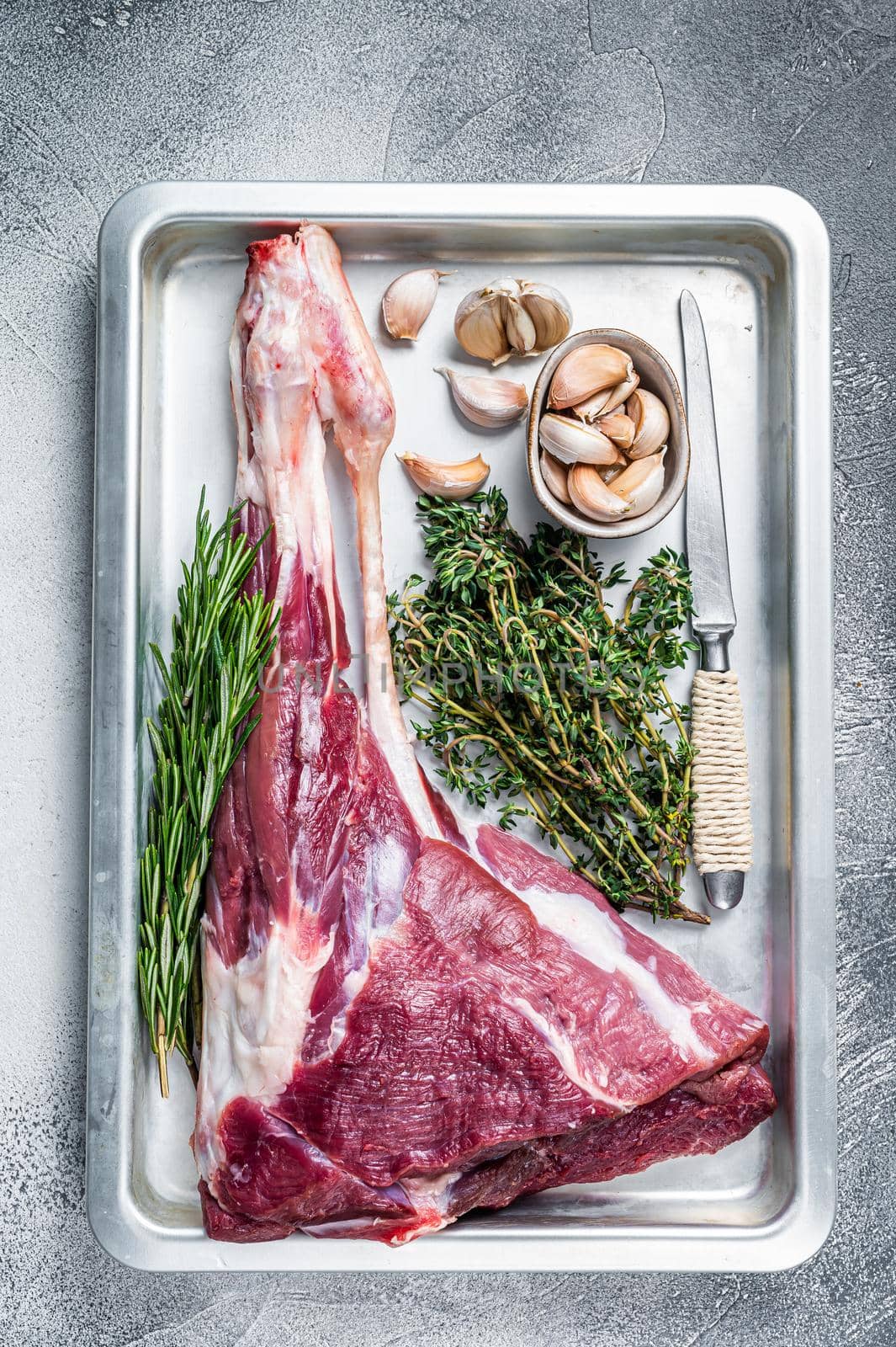 Uncooked Raw goat or lamb leg with herbs in baking tray. White background. Top view by Composter